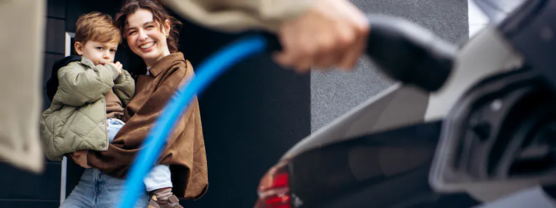 Mother holding young boy watching husband plug EV charger into car
