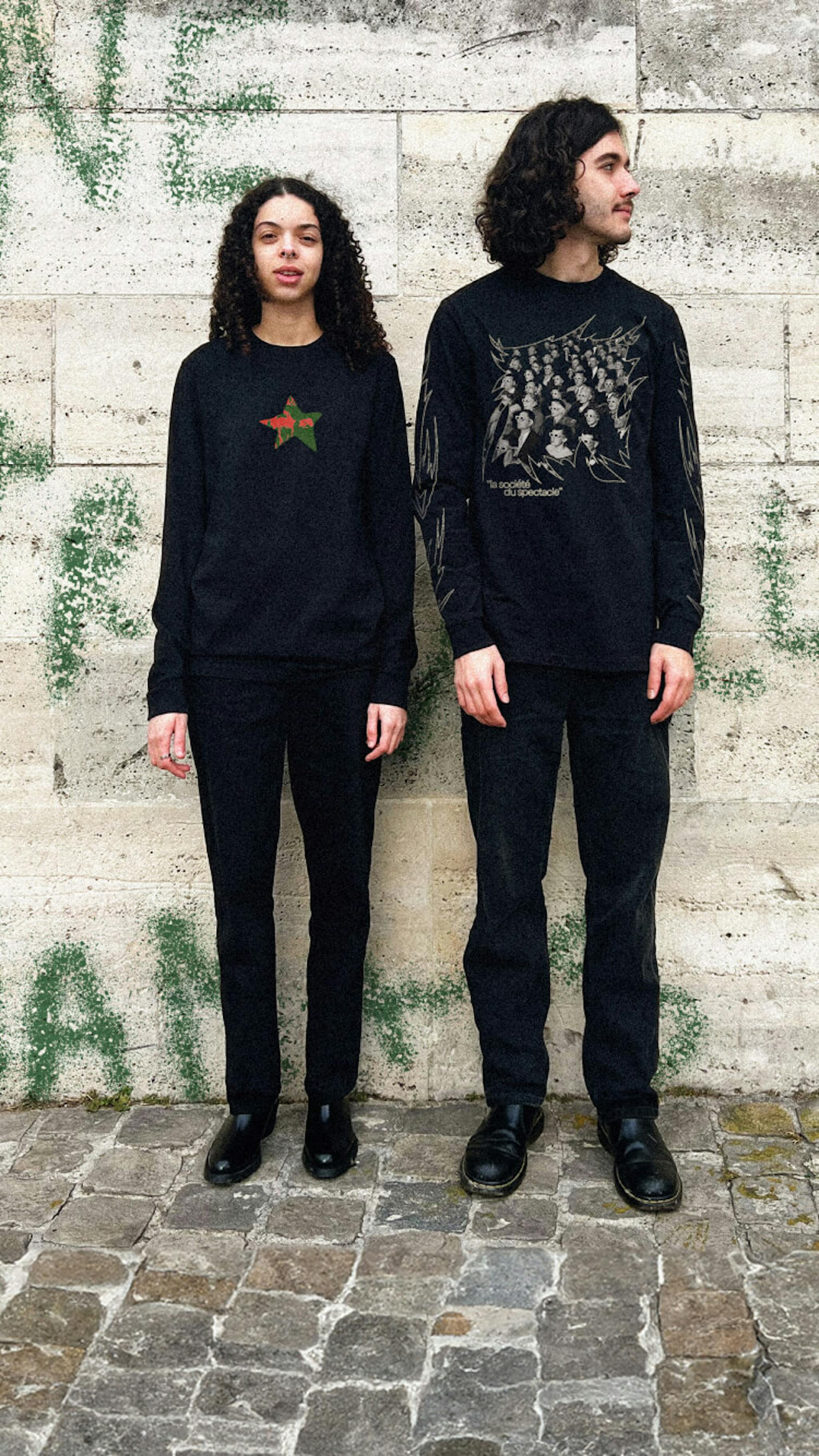 Two individuals in black attire against a graffitied wall.