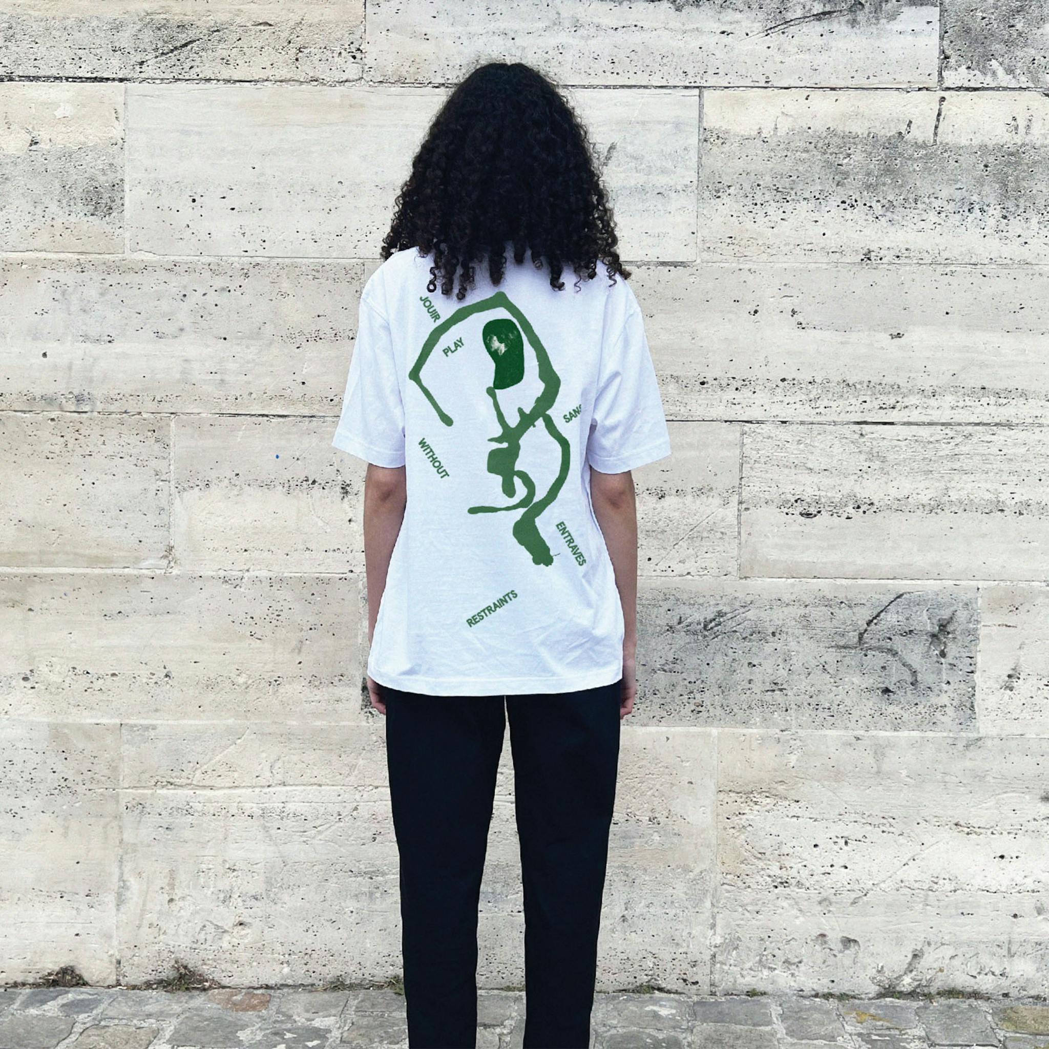 A woman with long dark hair wearing a white t-shirt with a green abstract graphic and the words placed around on the back. 
