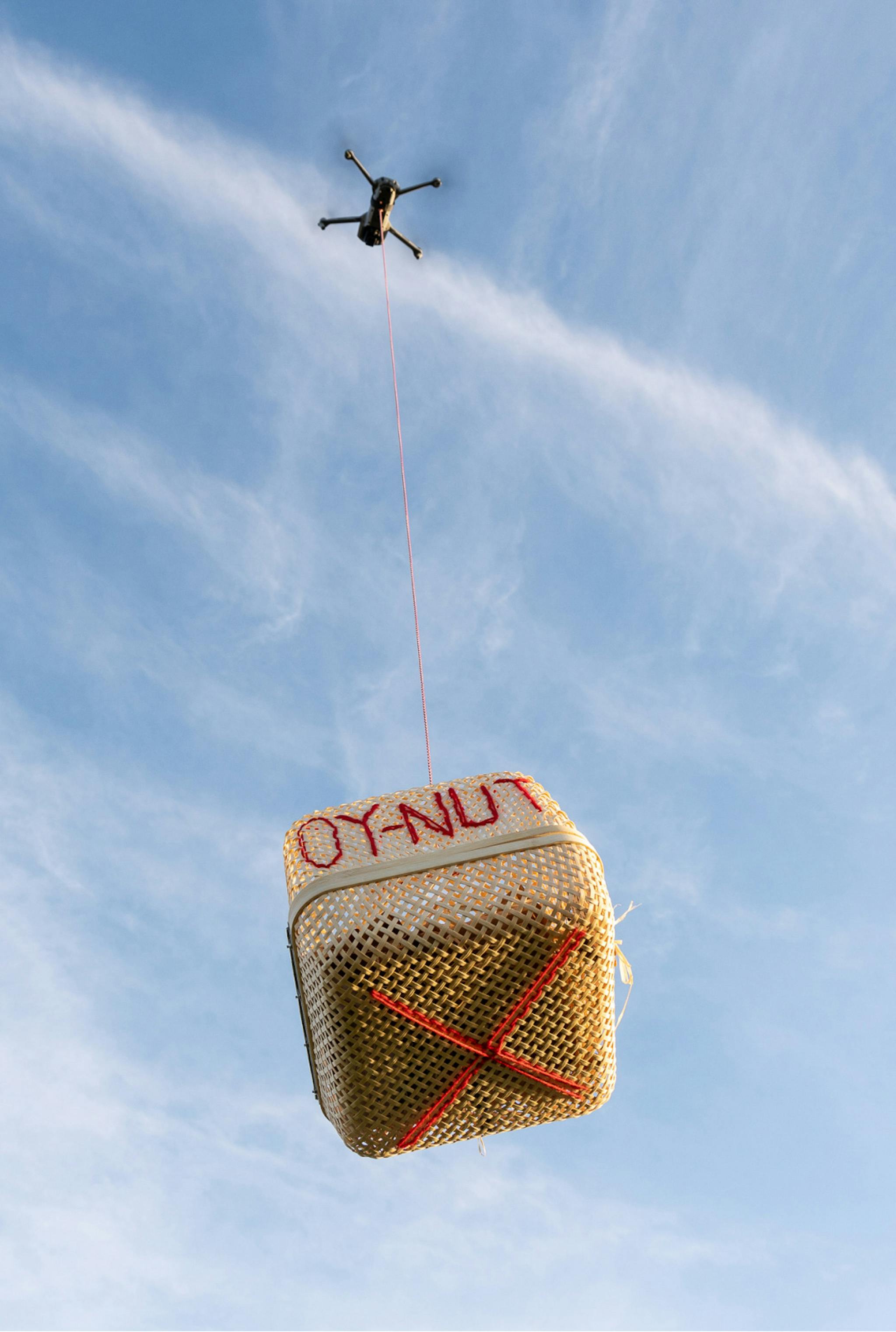 A close up of a basket in the air being lifted by a drone. 