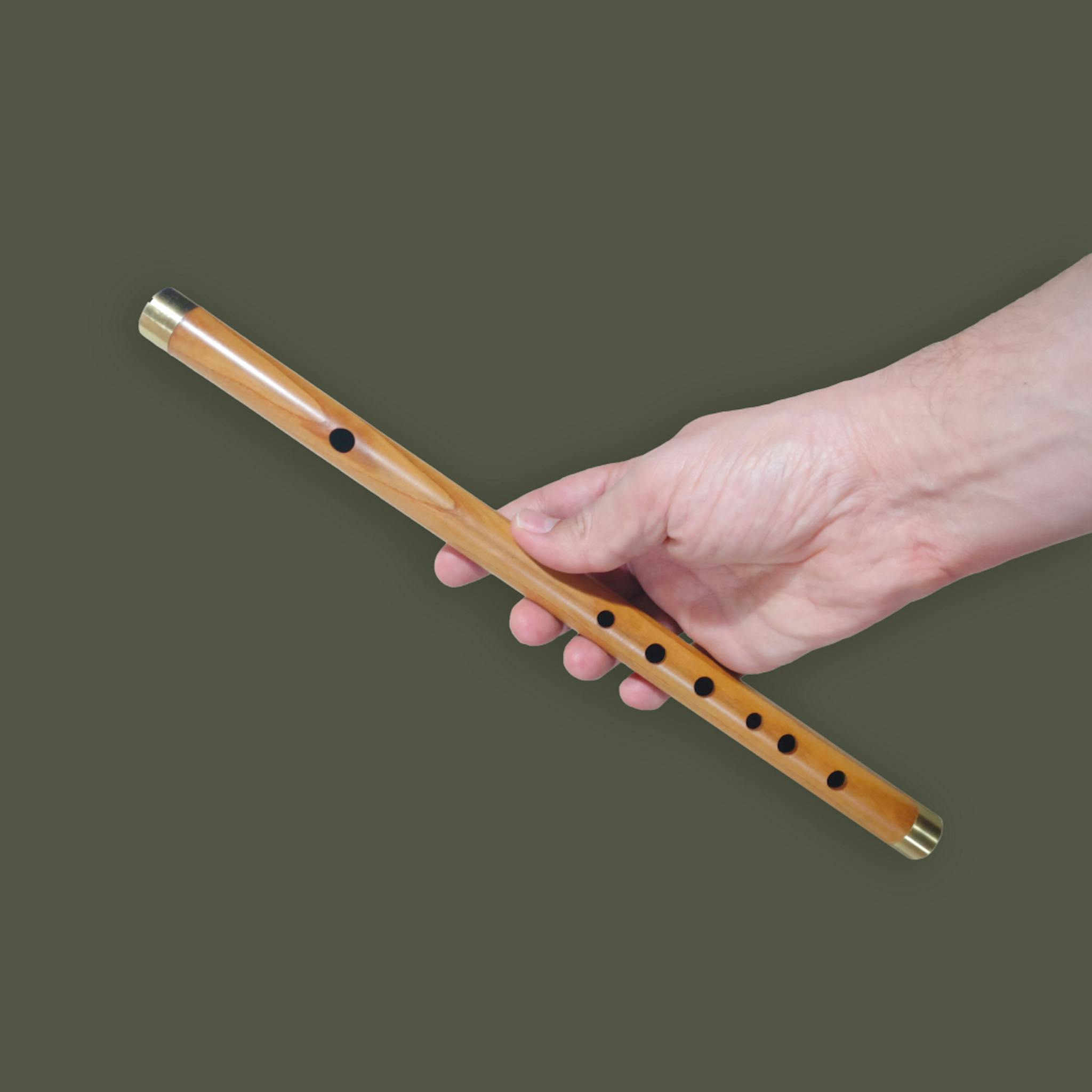 A wooden flute being held by a hand on a green backdrop.