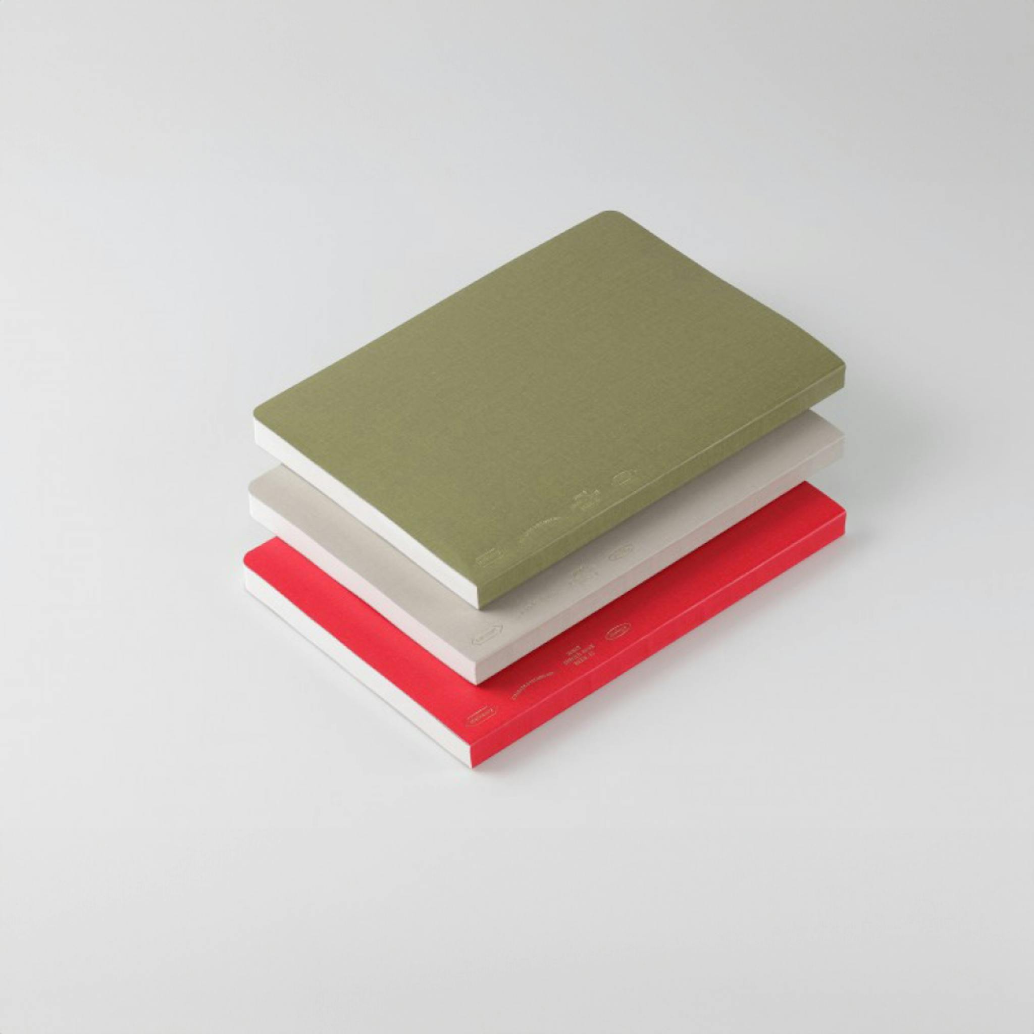 A stack of three notebooks. From top to bottom they are green, grey, and red. 