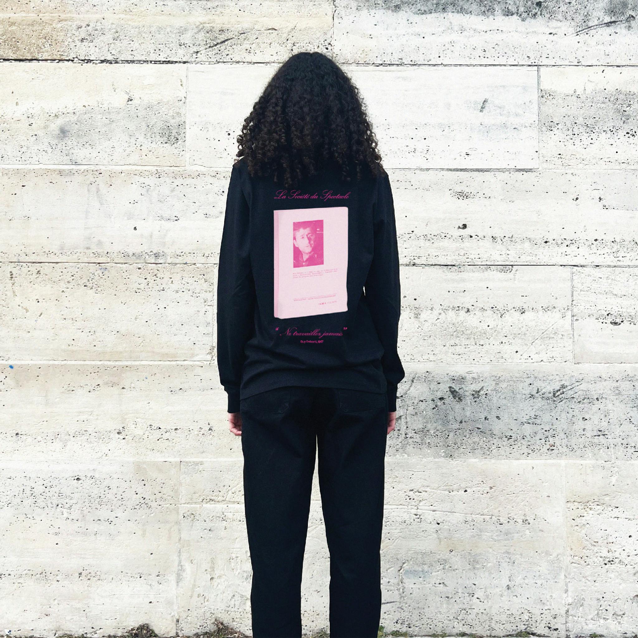 A woman with long dark hair wearing a black long-sleeve T-shirt with large pink book graphic on the back and french words over and underneath.