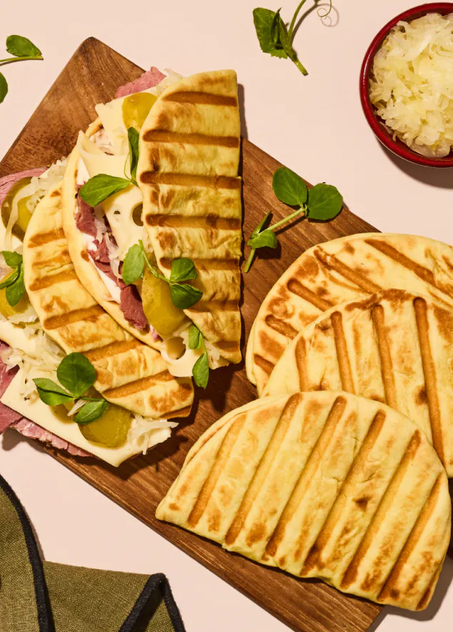 Folded brioche style flatbreads filled with smoked ham and cheese plus on a bread board on pink back drop