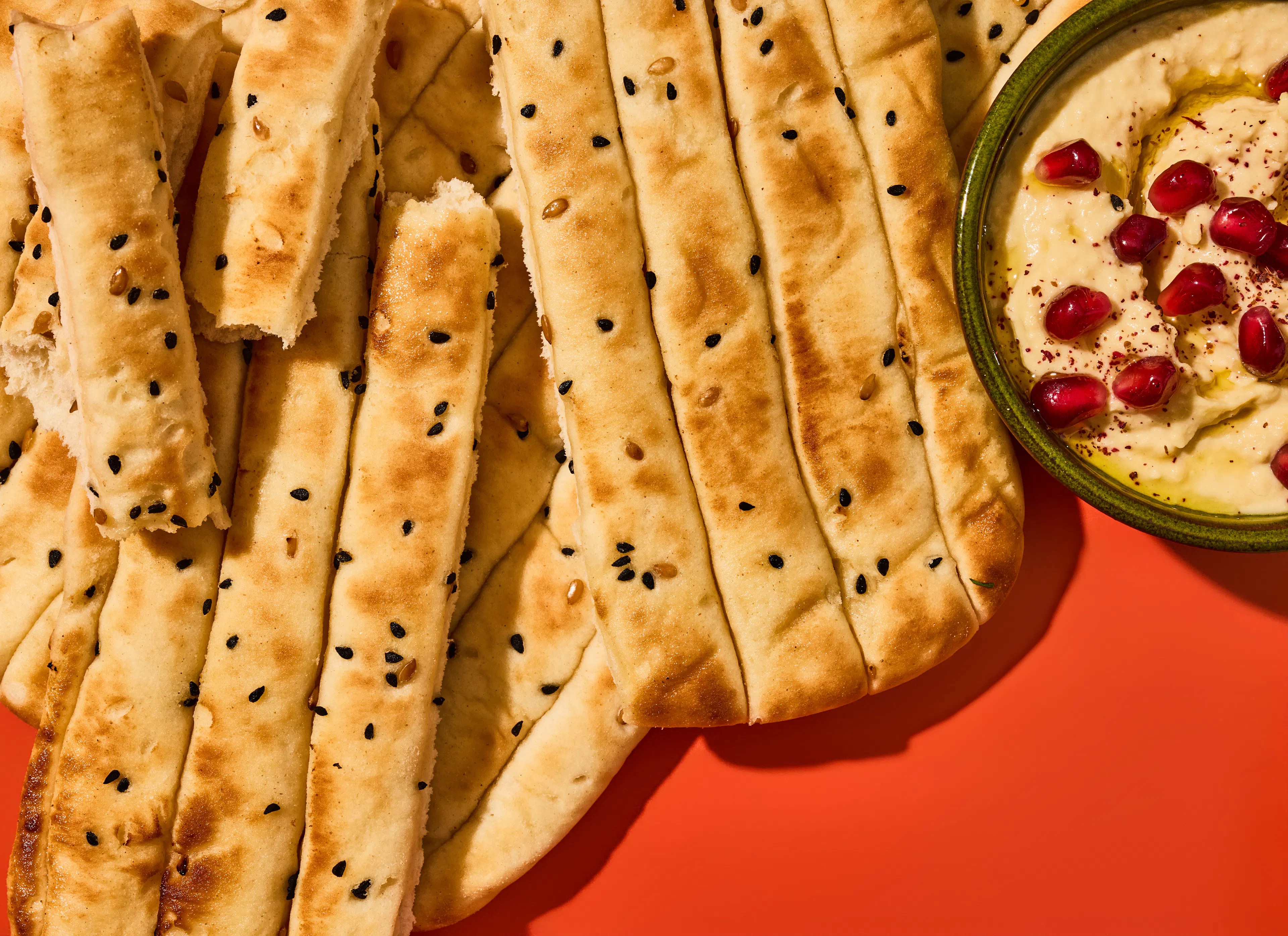 Torn sharing flatbreads on a red background with a small bowl of humous