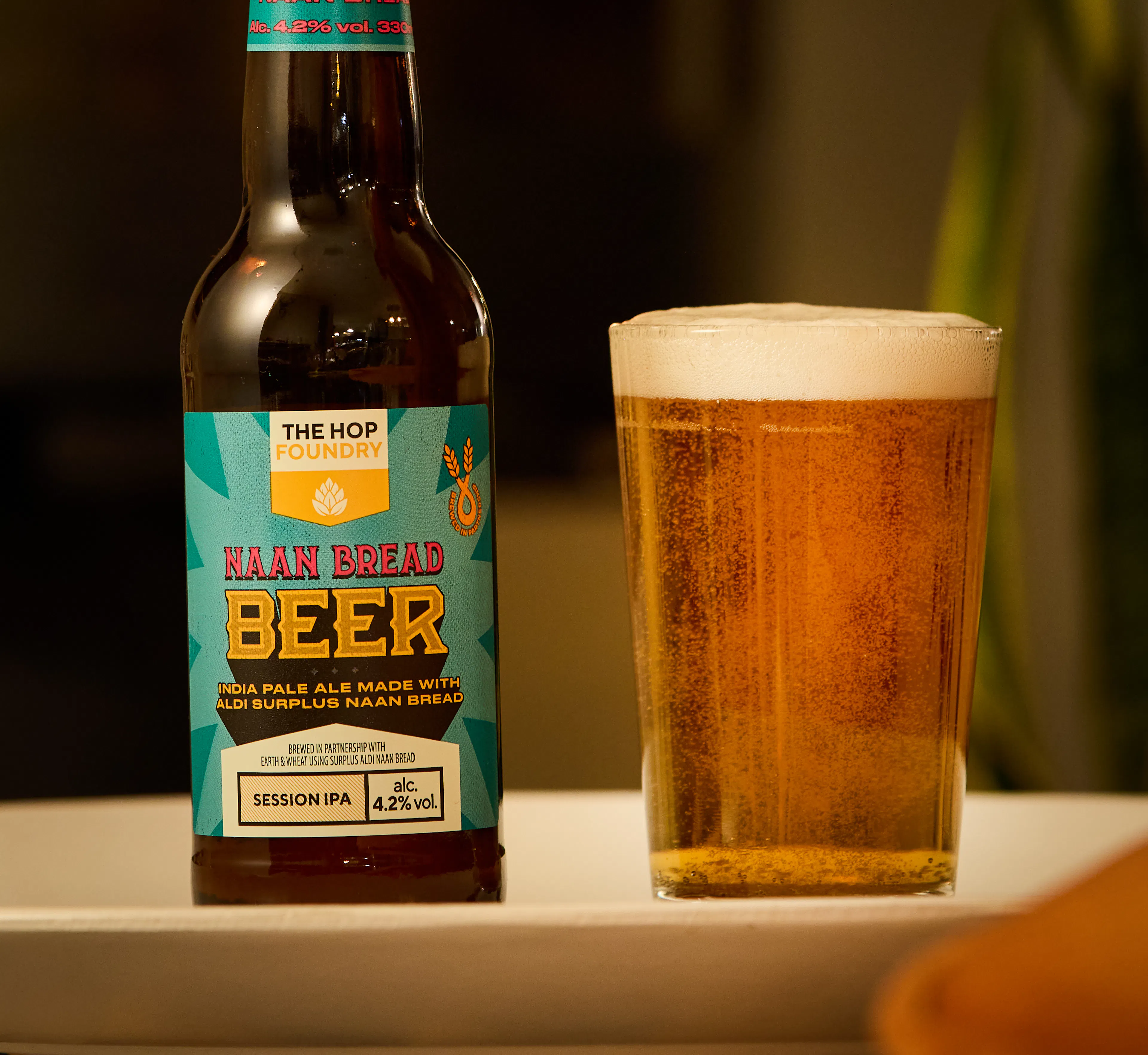 Earth & Wheat IPA in a bottle next to a full beer glass