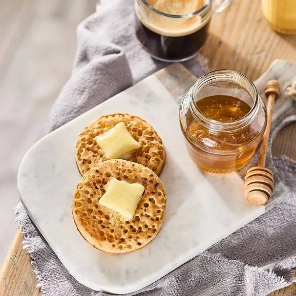 2 crumpets on a white plate with honey and butter topping