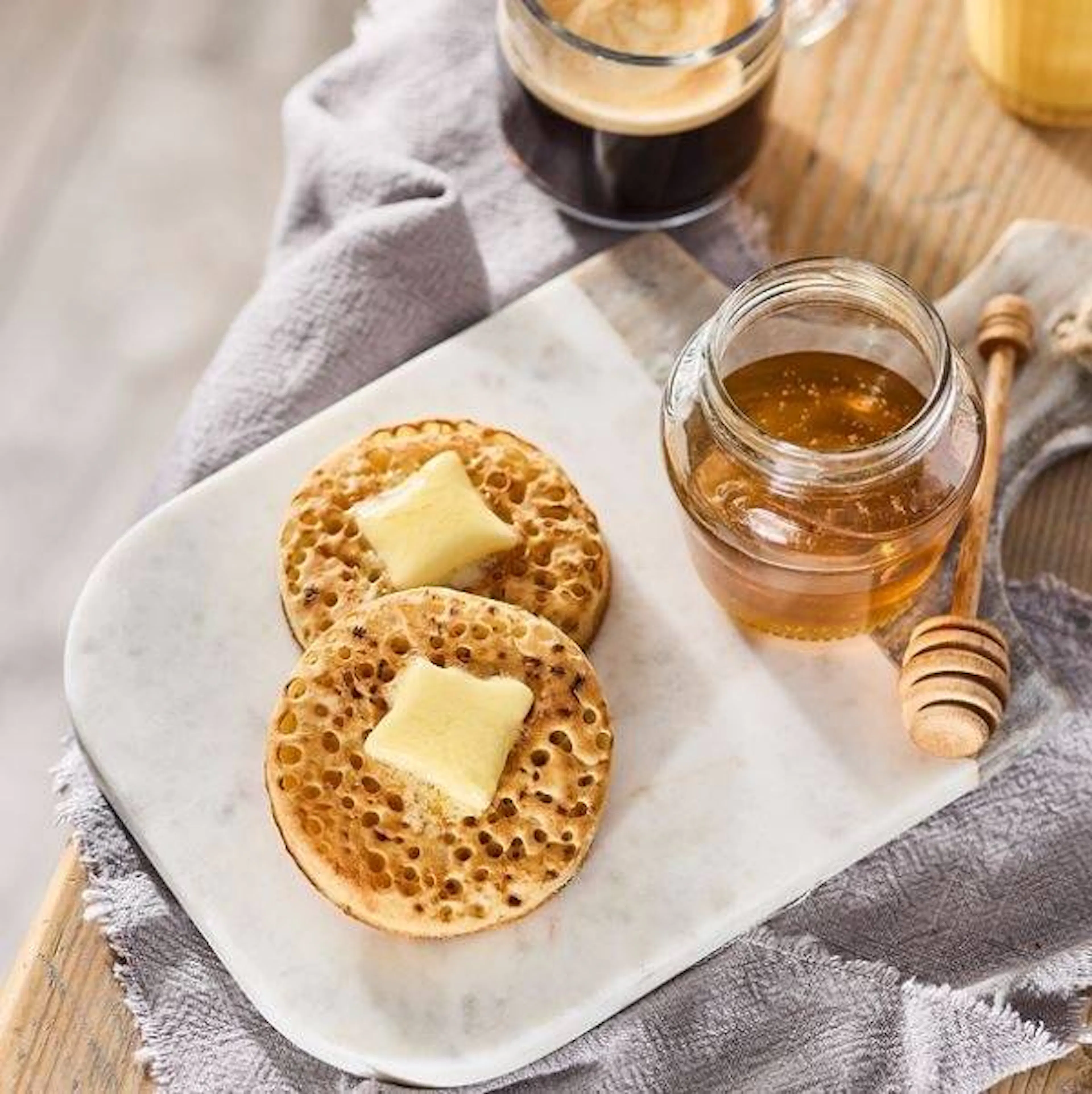 2 crumpets on a white plate with honey and butter topping
