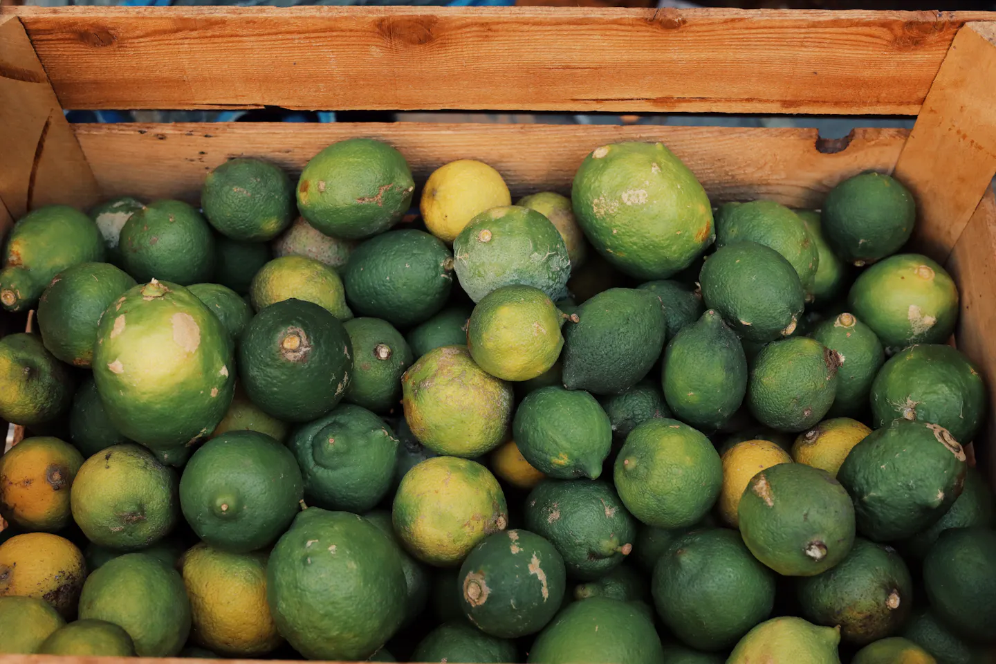 A wooden crate of green and yellow lemons on a southern Italian market stall