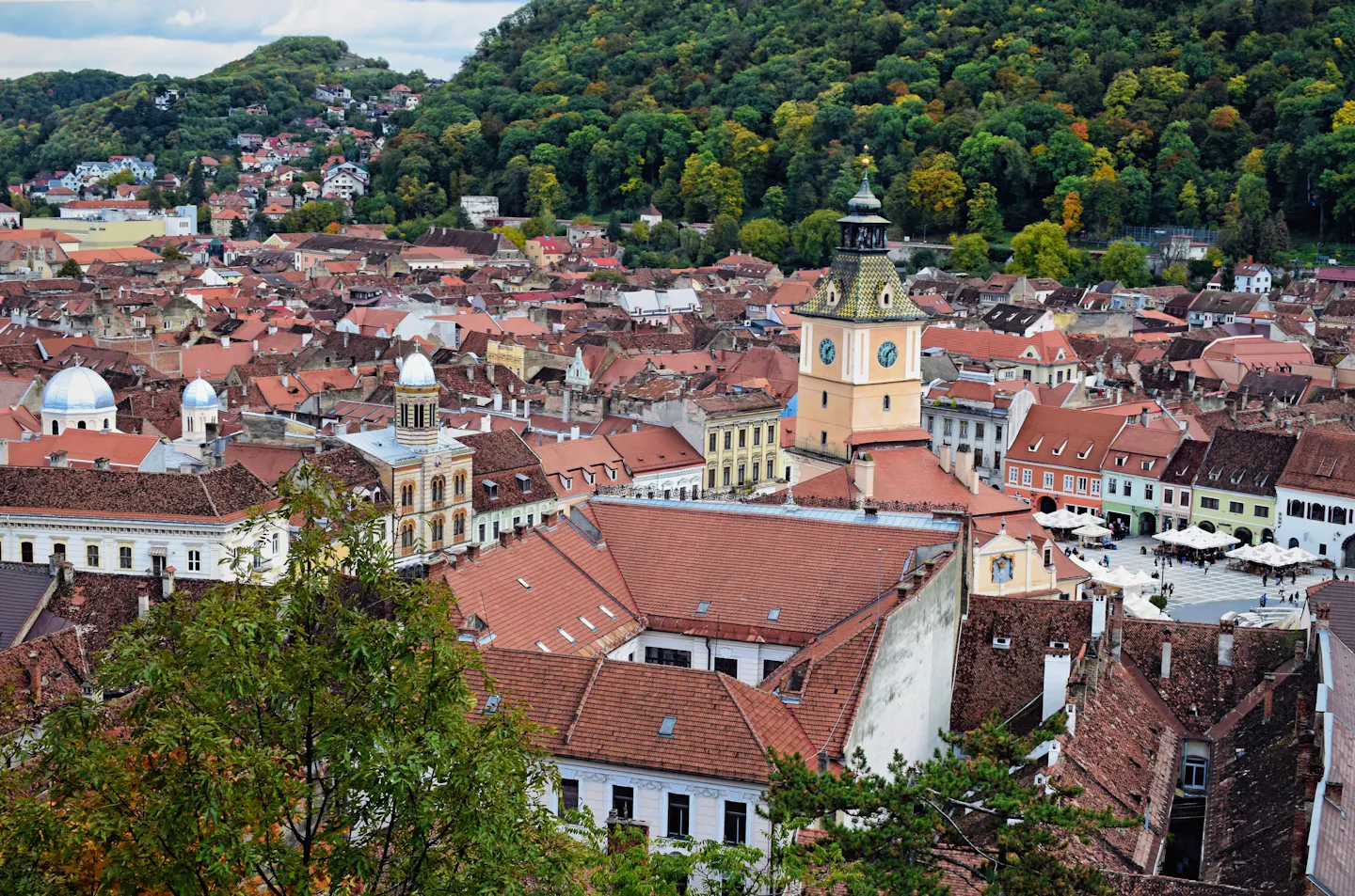 Aerial view of Brașov's old town and clock tower below green hills