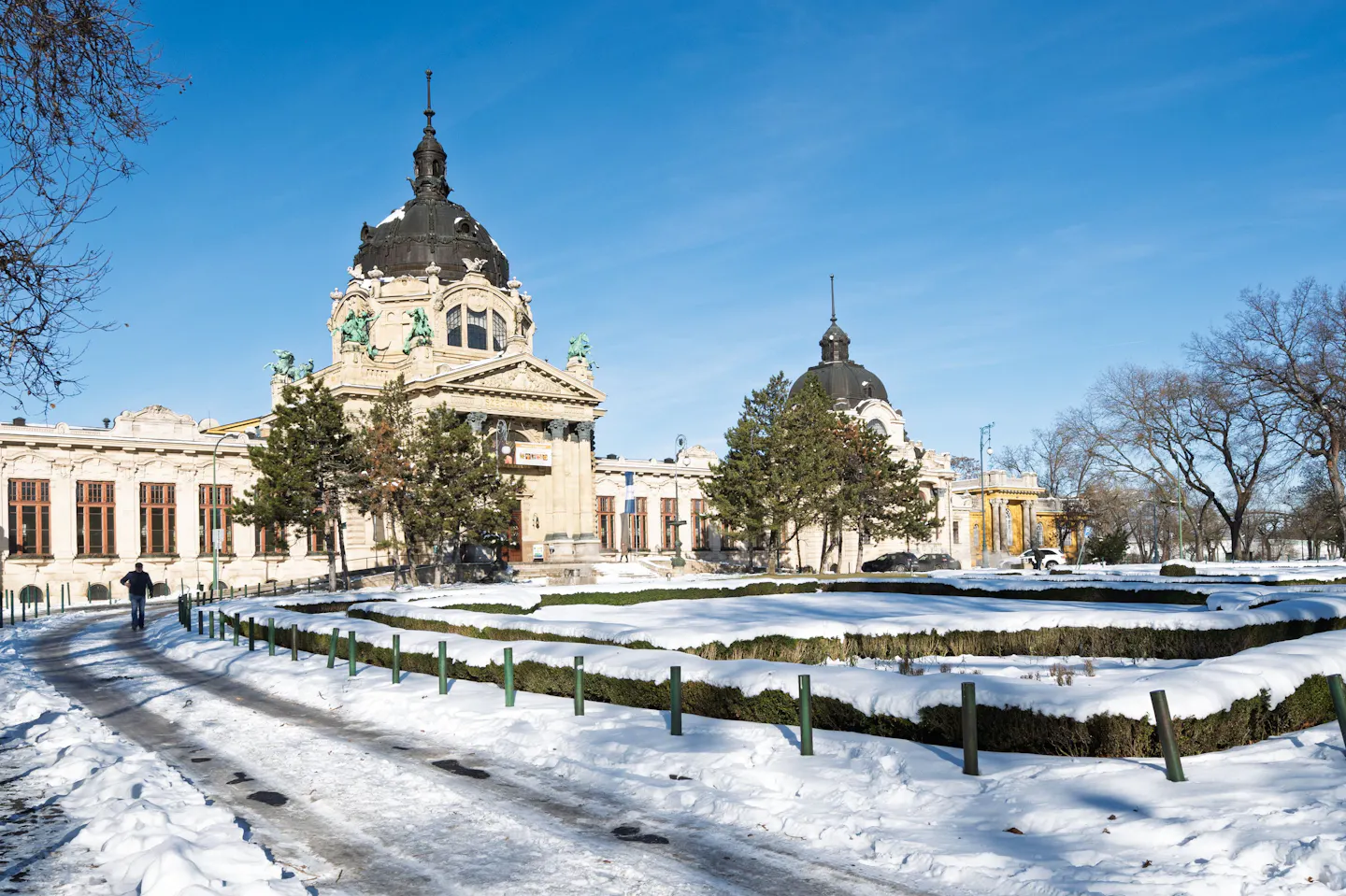 The yellow facade of the Szechenyi thermal baths in Budapest above snow-covered gardens