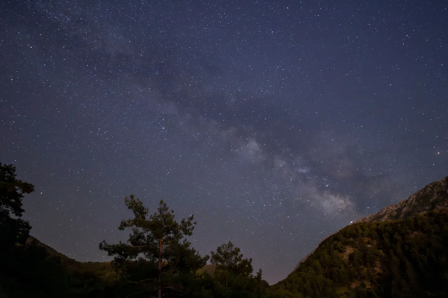 The band of the Milky Way running across a dark blue night sky above forested mountain ridges