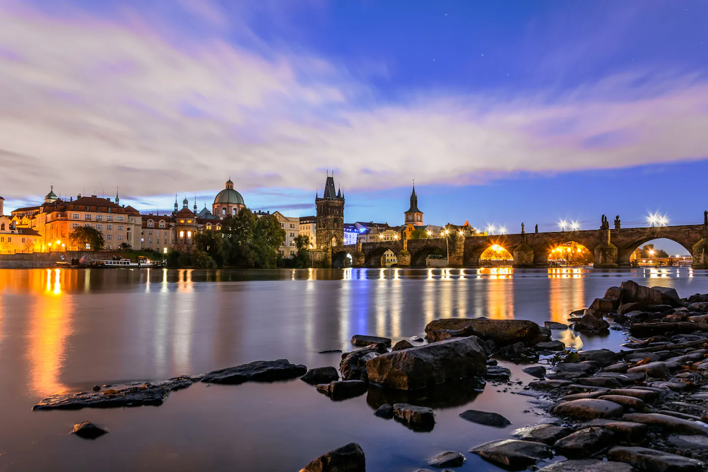 Charles Bridge and the lit towers of Prague's Old Town reflected in the Vltava at blue hour