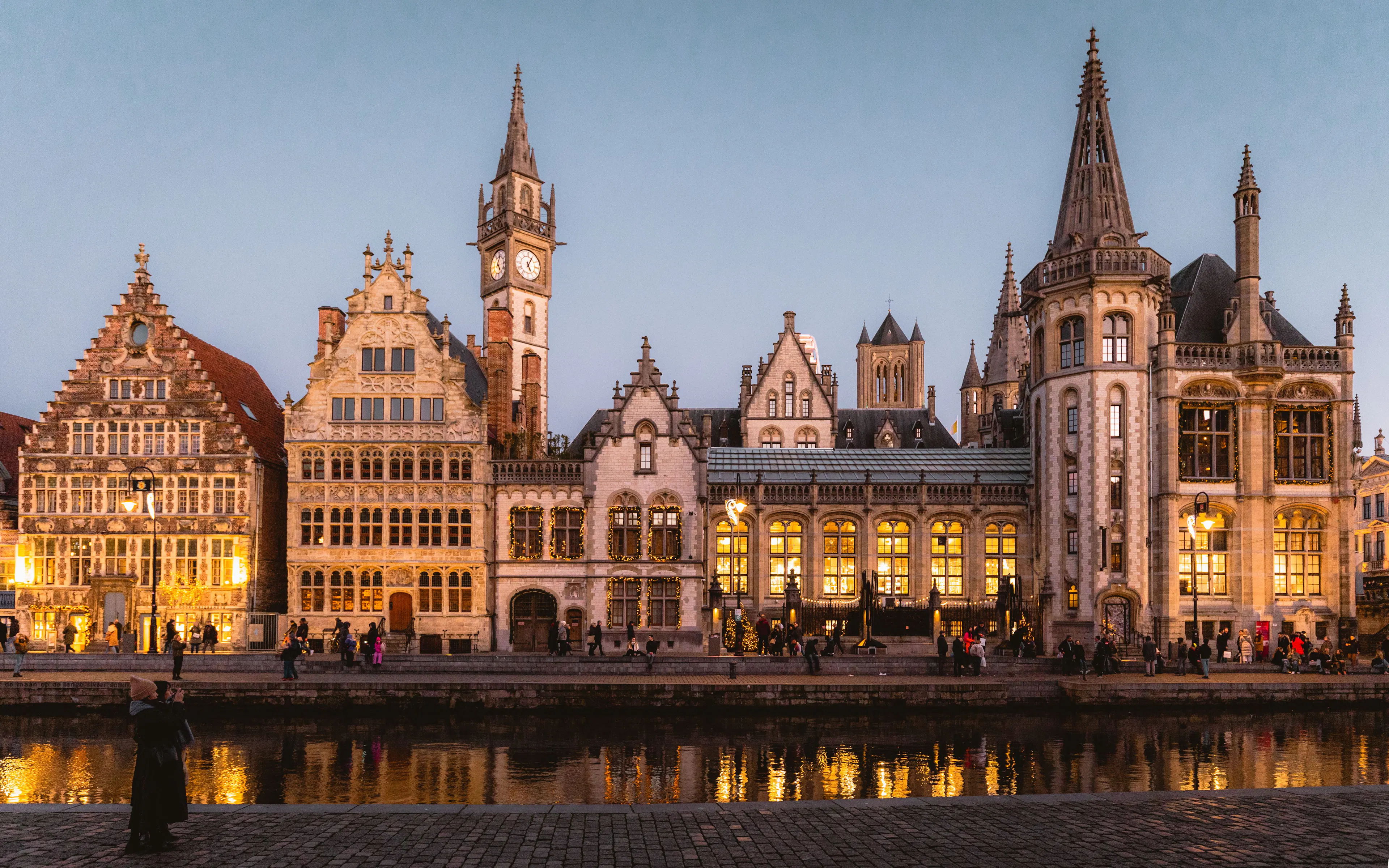 The medieval guild houses of Graslei in Ghent lit gold at twilight and reflected in the canal