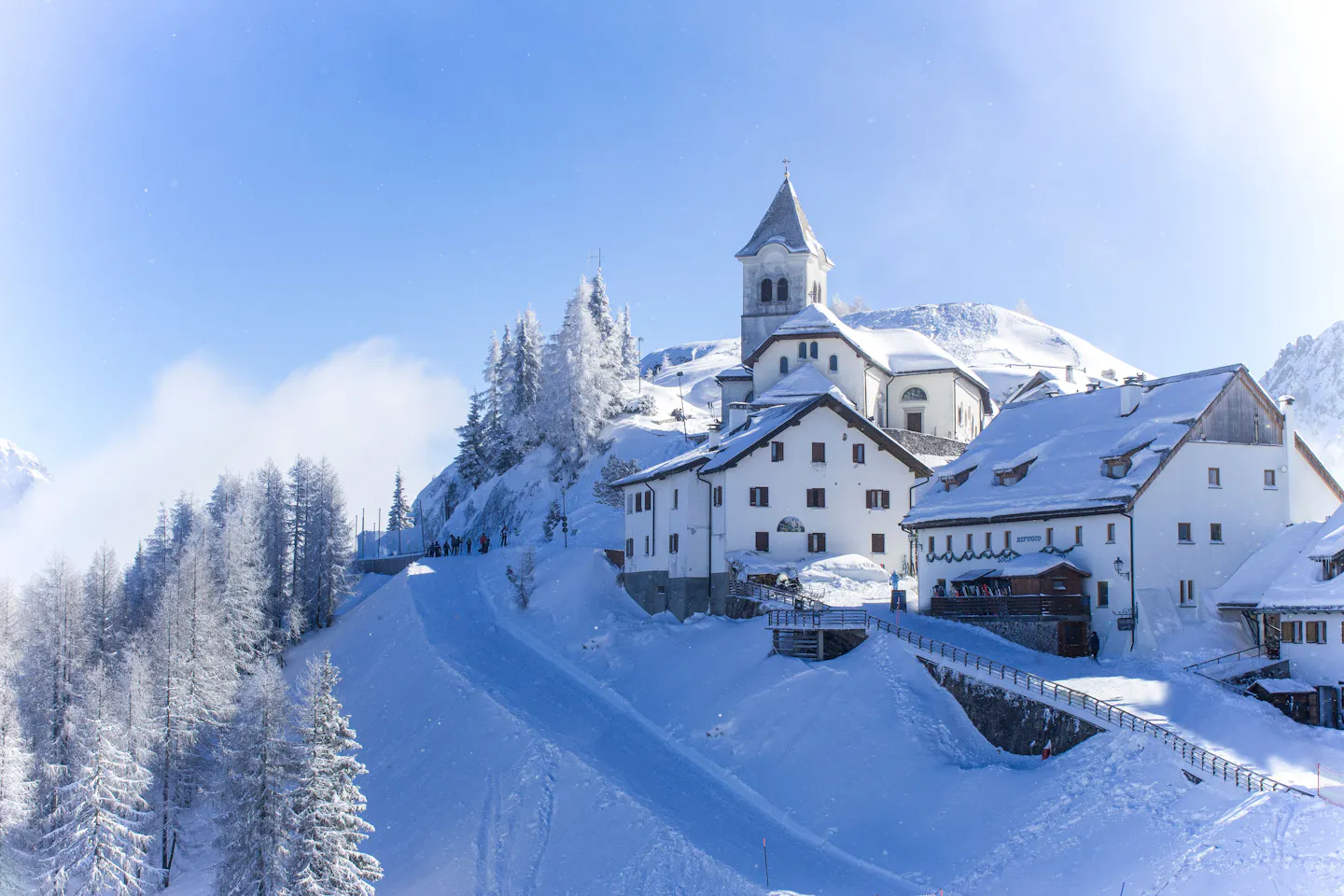 A snow-covered Alpine village and church tower on a ridge under a blue winter sky