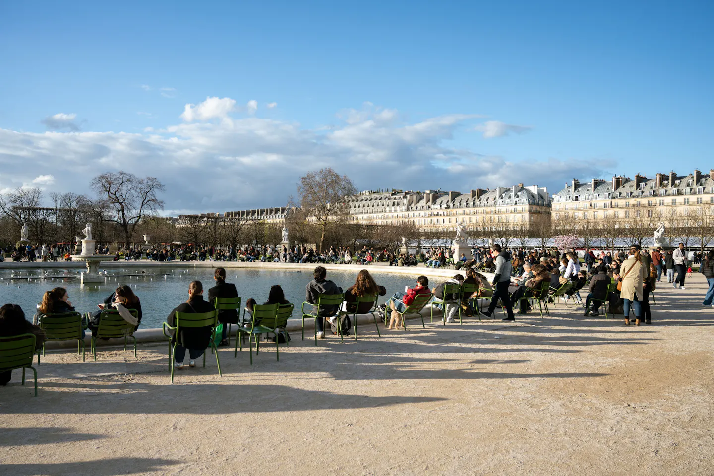 Green metal chairs around the octagonal basin in the Tuileries Garden under a bright blue sky