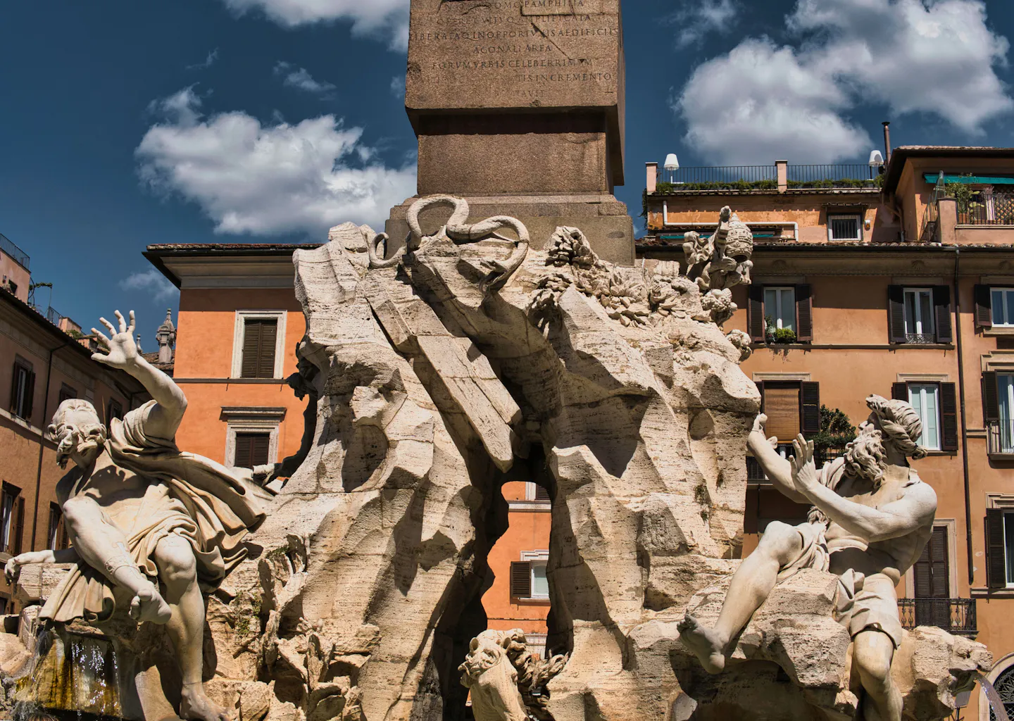 The marble river gods and obelisk of Bernini's Fountain of the Four Rivers against a deep blue sky in Piazza Navona