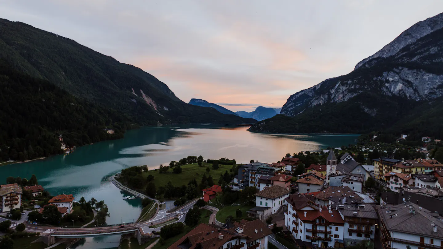 An Alpine lake town at dusk with pink cloud reflected in still turquoise water