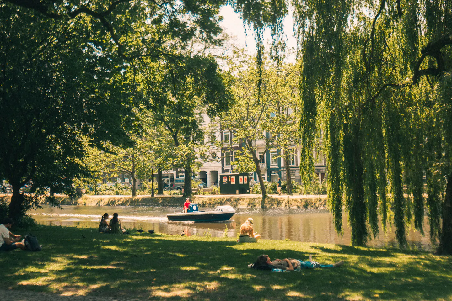 People resting on the grass under willows beside a pond in Amsterdam's Vondelpark