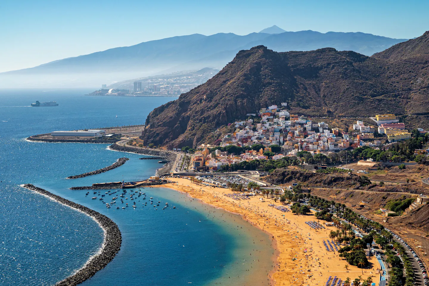 An aerial view of Playa de Las Teresitas in the Canary Islands, Spain, with a sandy bay, breakwaters and steep mountains.