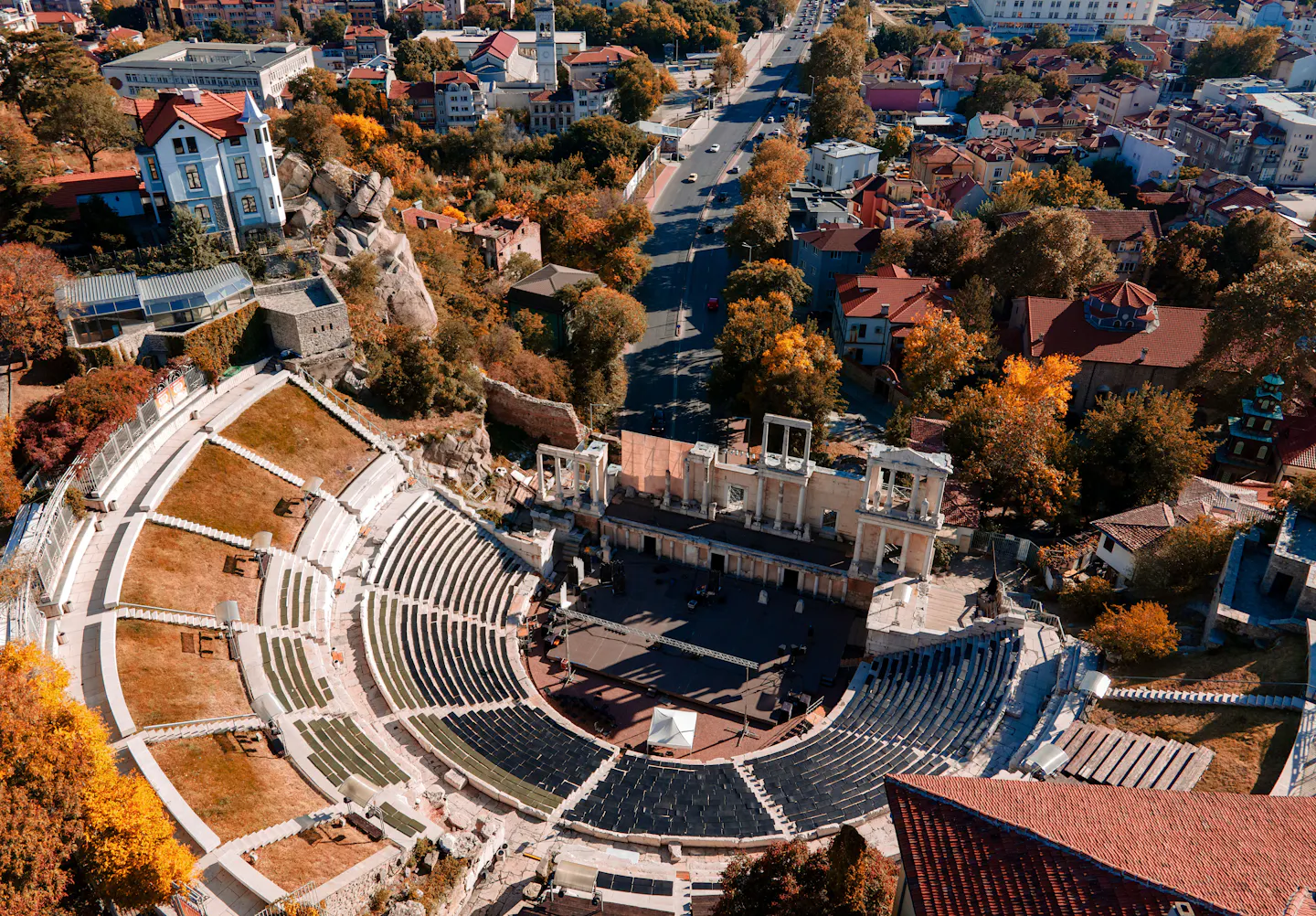 The Roman theatre of Philippopolis seen from above, ringed by autumn trees and red rooftops in Plovdiv