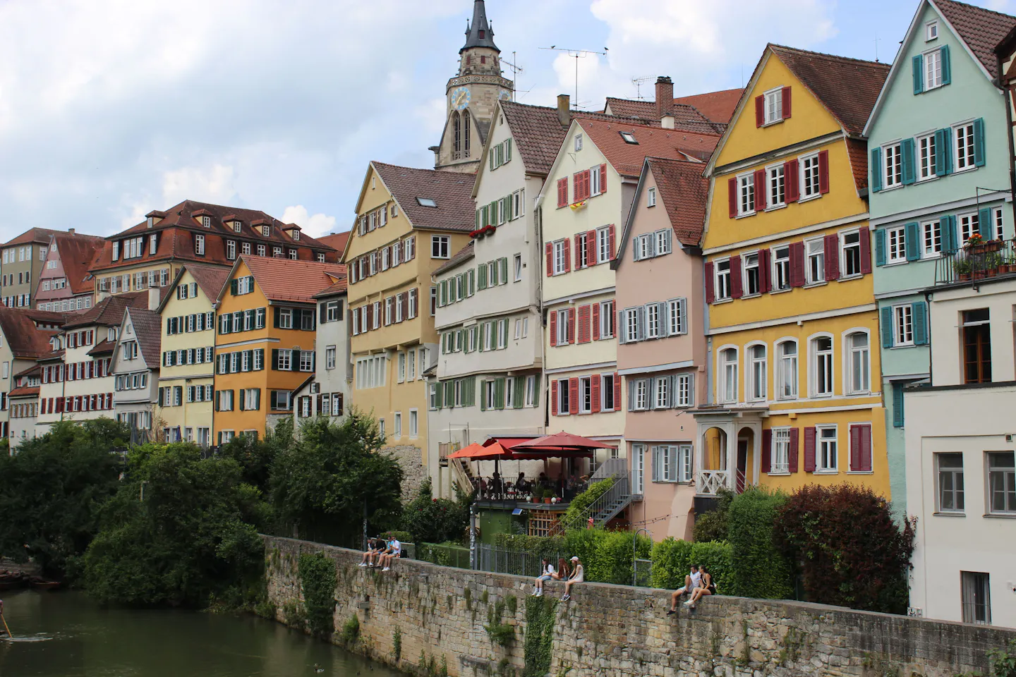 Pastel half-timbered houses stacked above the Neckar riverbank in Tubingen under a summer sky