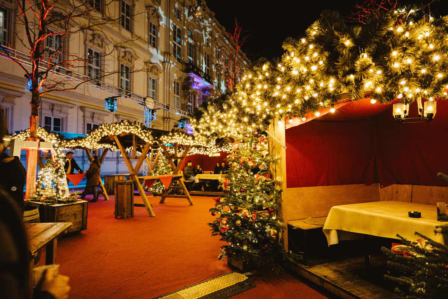 Wooden Christmas market huts and a lit tree glowing under strings of lights at night