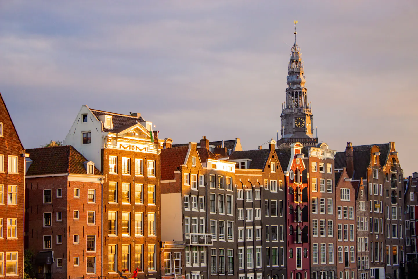 Amsterdam's stepped canal-house gables lit gold at sunset below a slender church tower
