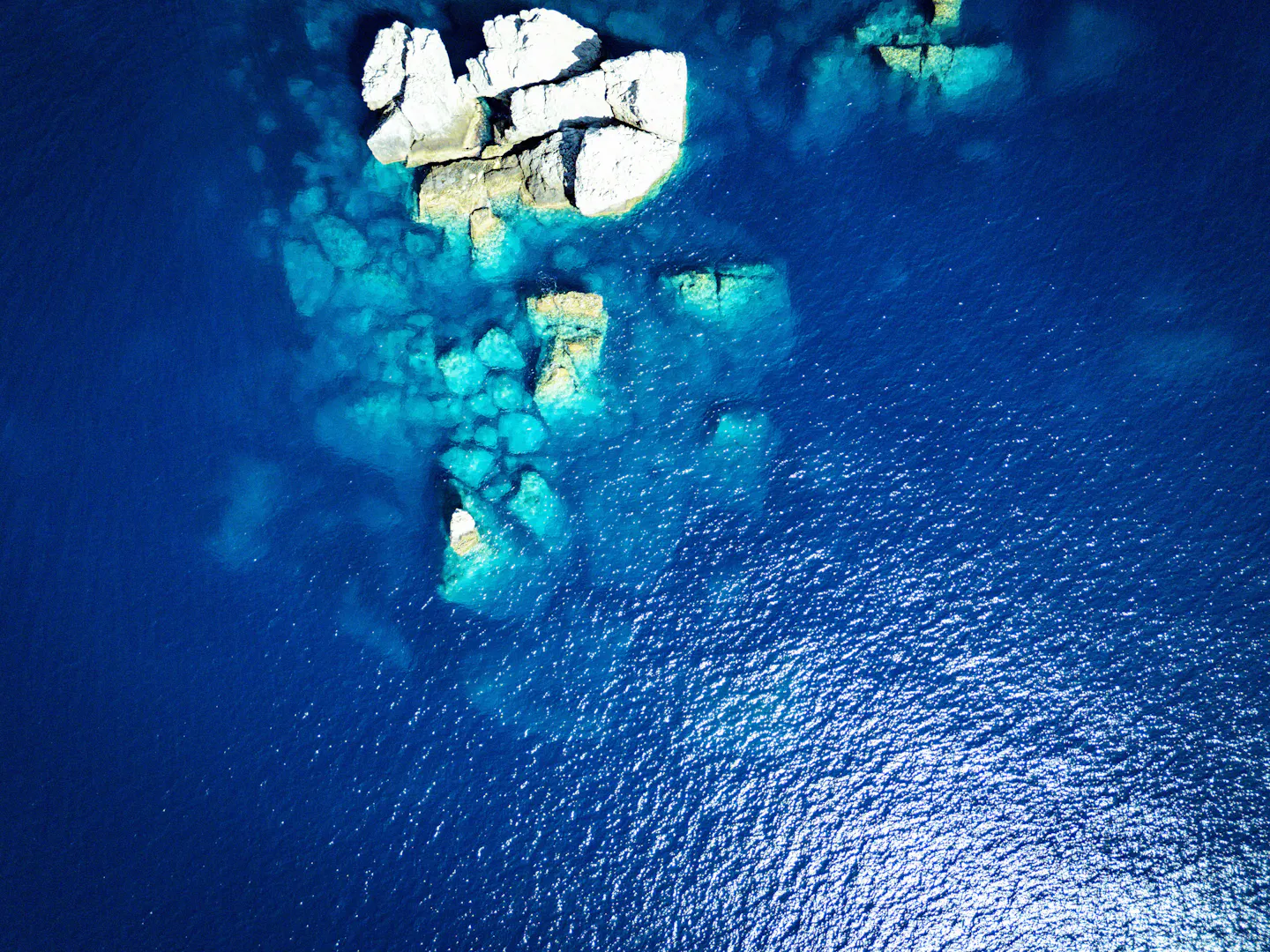 White rocks and turquoise shallows in deep blue Mediterranean water seen from above