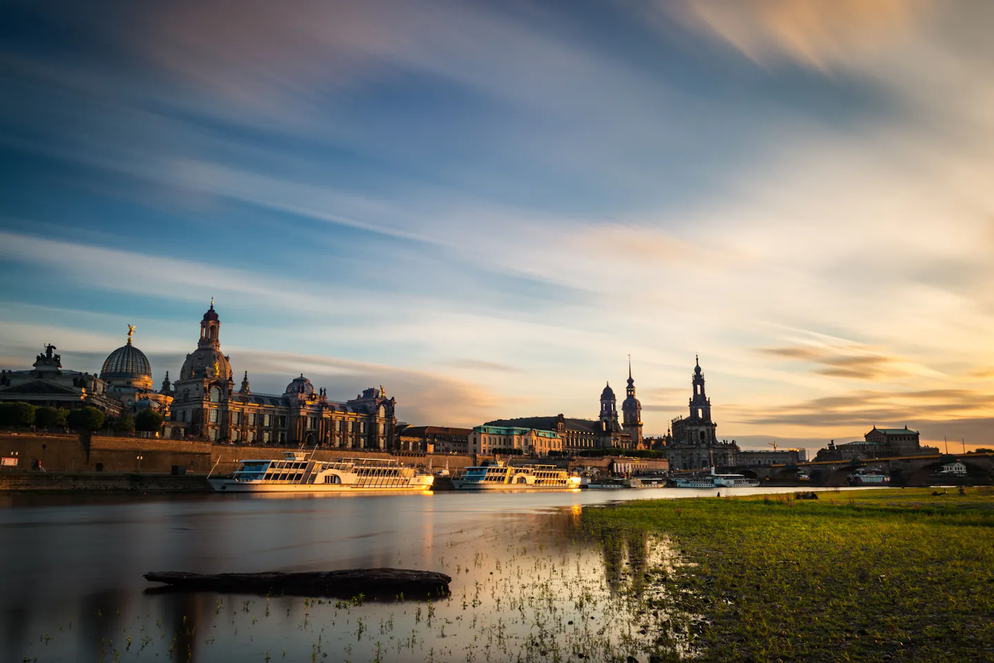 Dresden's domes and towers along the Elbe under a wide streaked sunset sky