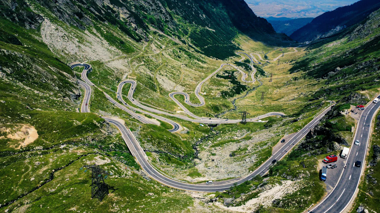 Aerial view of a winding mountain road crossing a steep green valley
