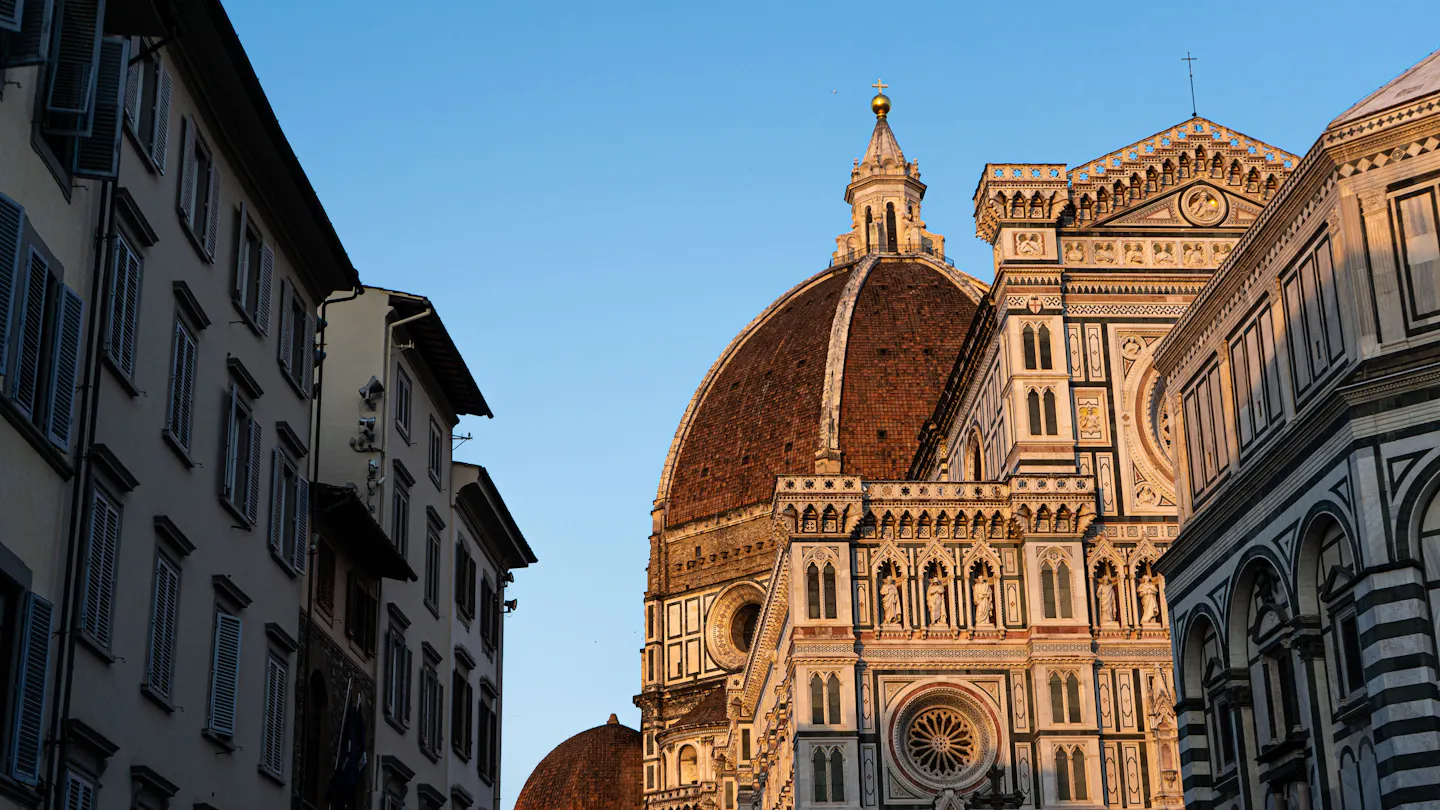 The dome and marble facade of Florence Cathedral catching golden evening light above a narrow street