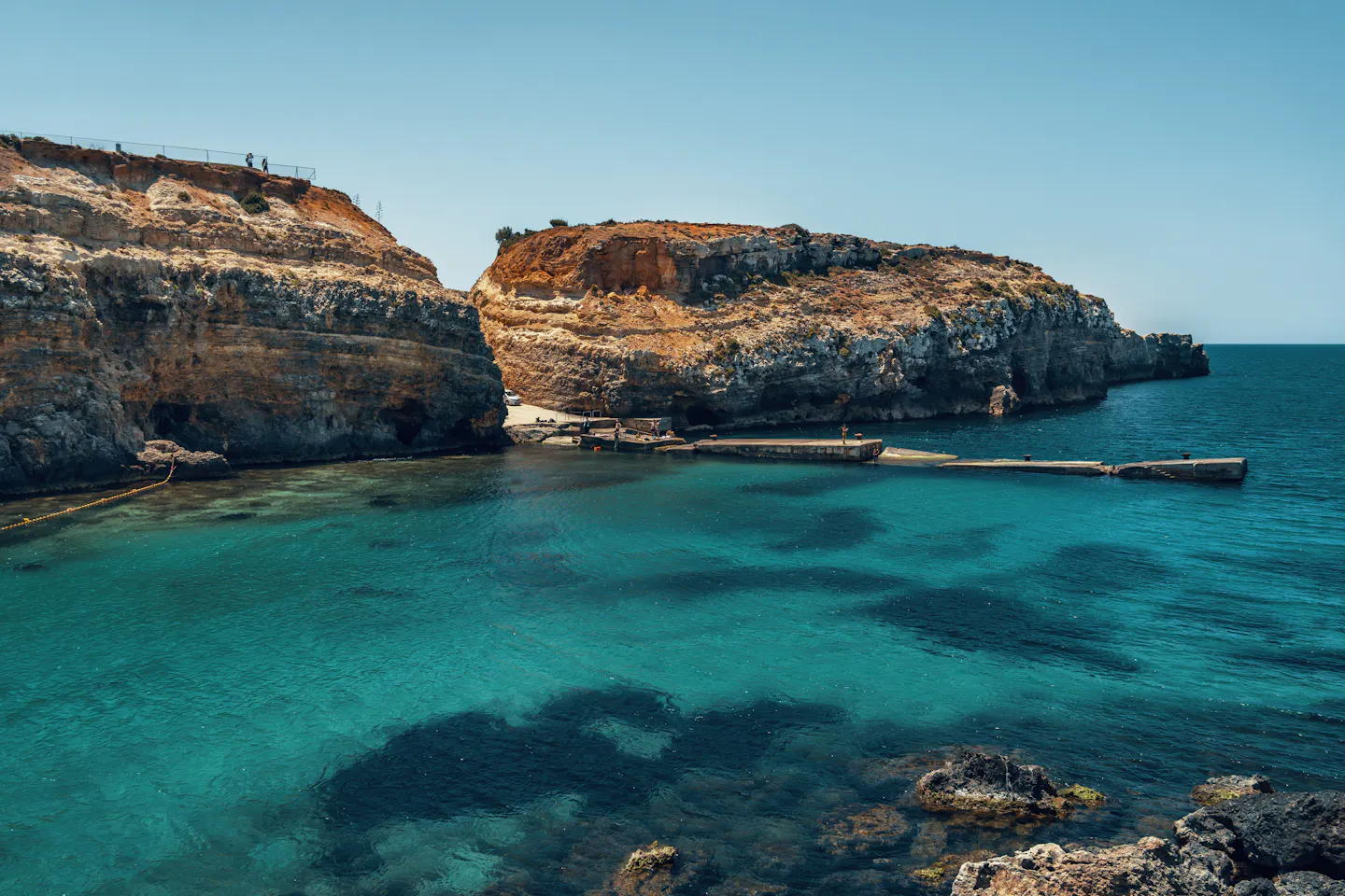 Clear turquoise water below ochre limestone cliffs on the coast of Gozo, Malta