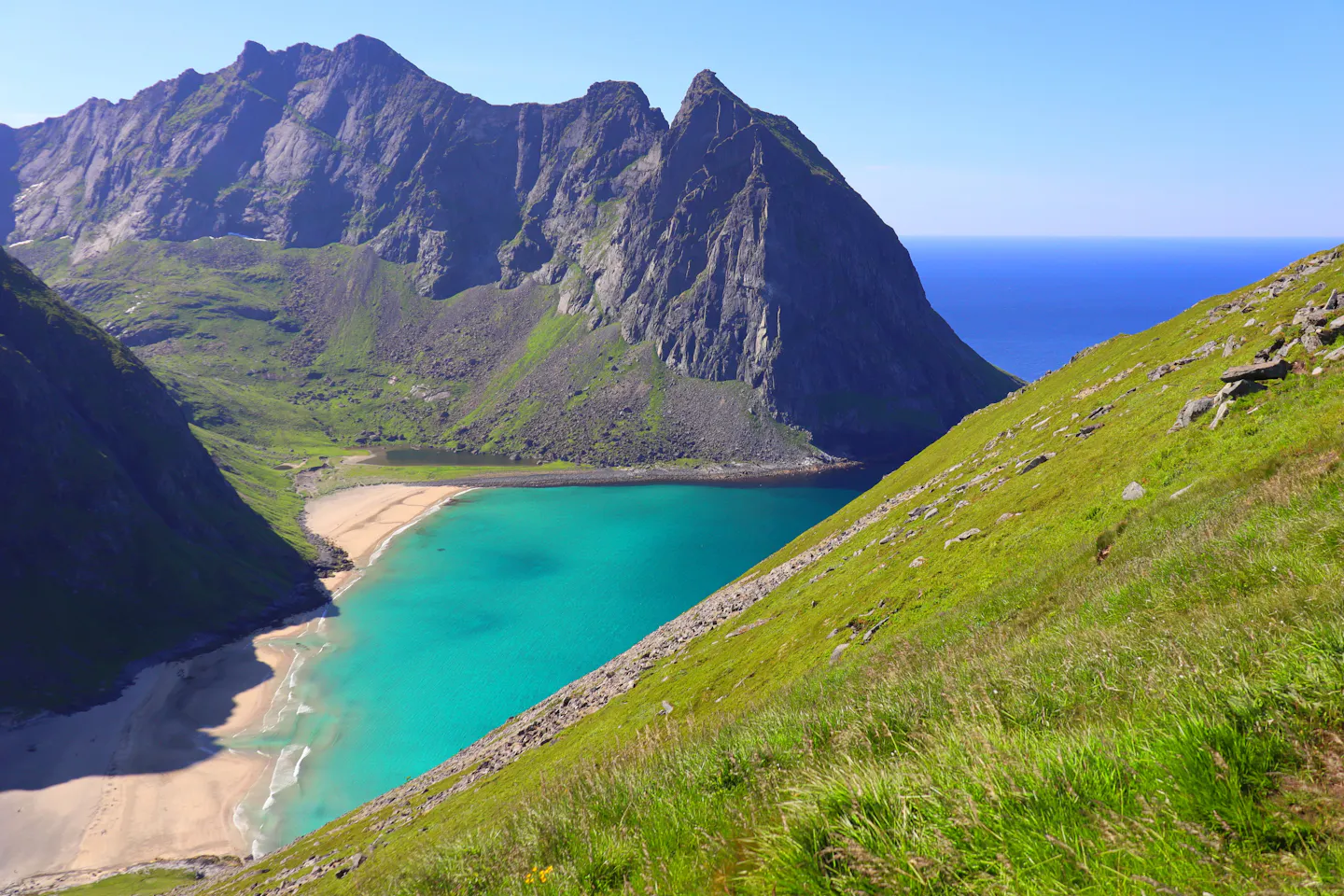A turquoise cove and empty pale-sand beach enclosed by steep granite peaks on the Norwegian coast