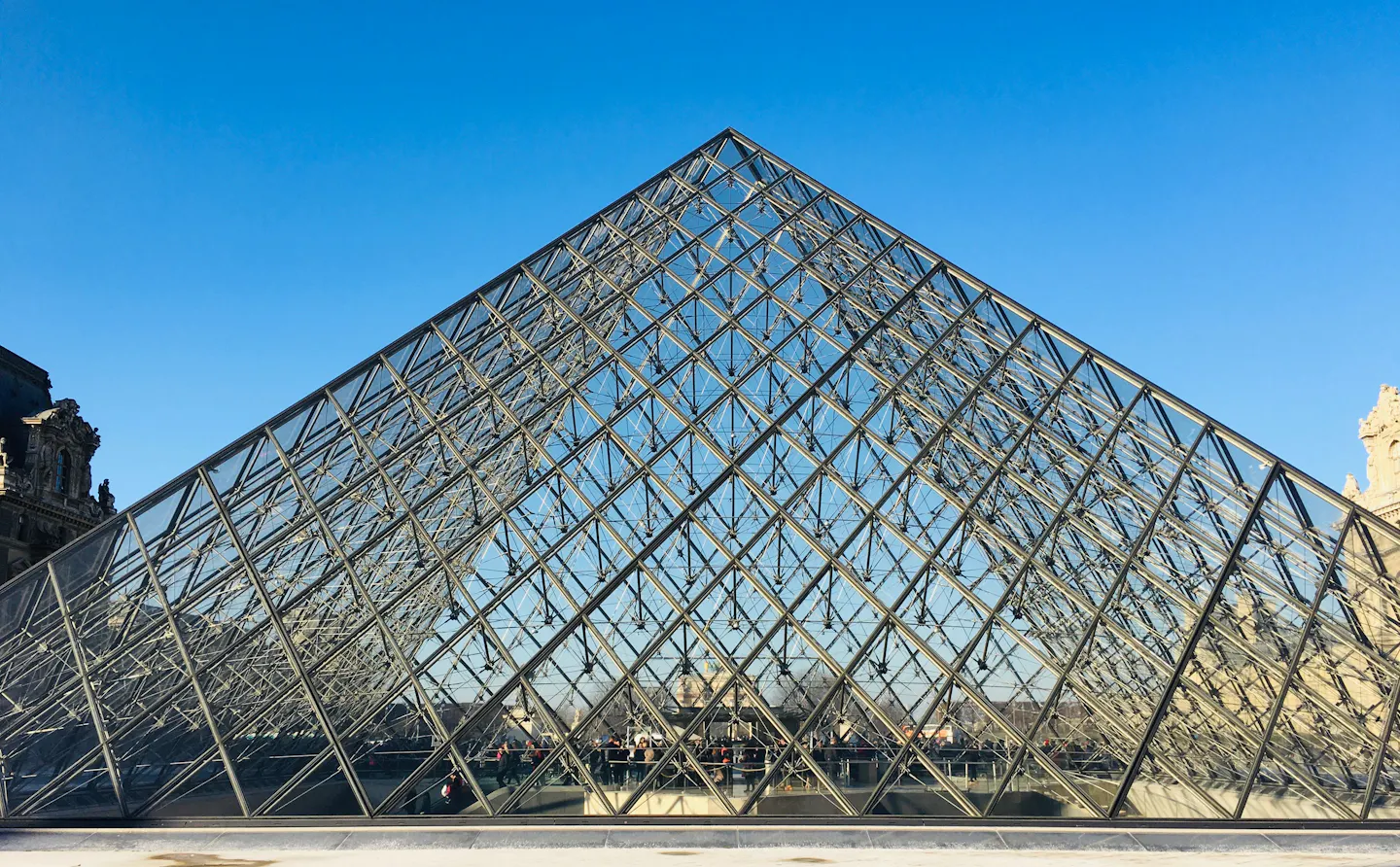 The glass and steel Louvre Pyramid seen straight on against a deep blue sky