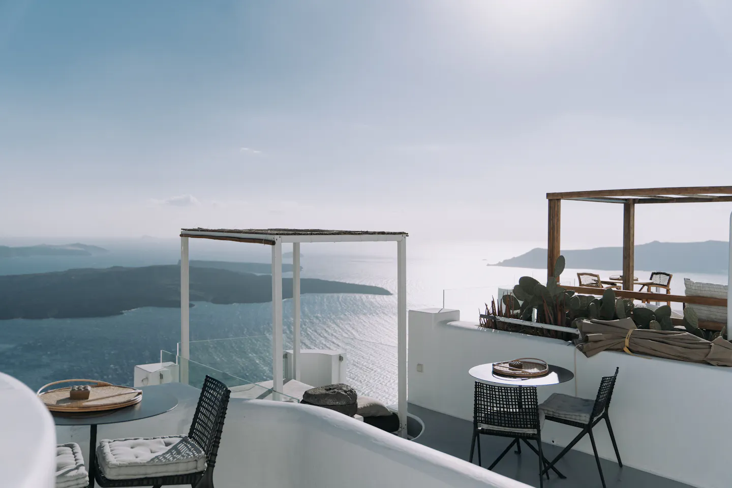 A whitewashed terrace with outdoor tables overlooking the blue sea and volcanic cliffs of Santorini