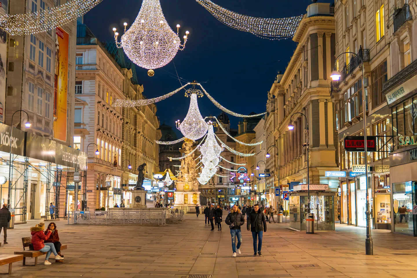 Festive chandelier lights above a historic shopping street in central Vienna at night