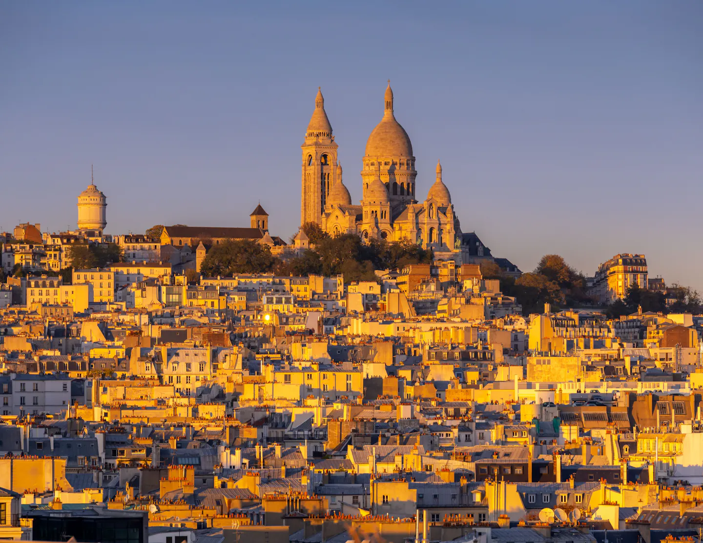 The domes of Sacre-Coeur rising above the rooftops of Montmartre in warm evening light