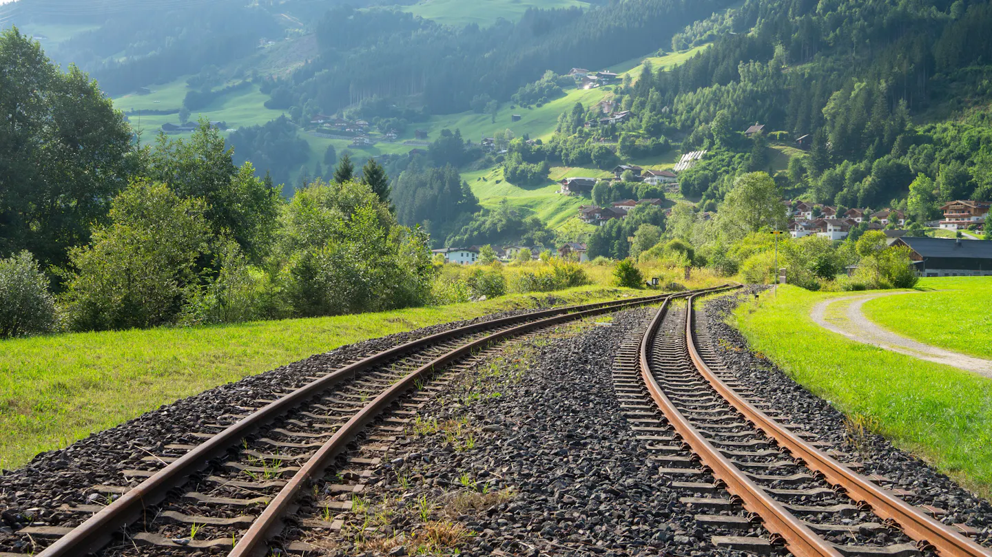 Railway tracks curving toward a green alpine valley scattered with farmhouses