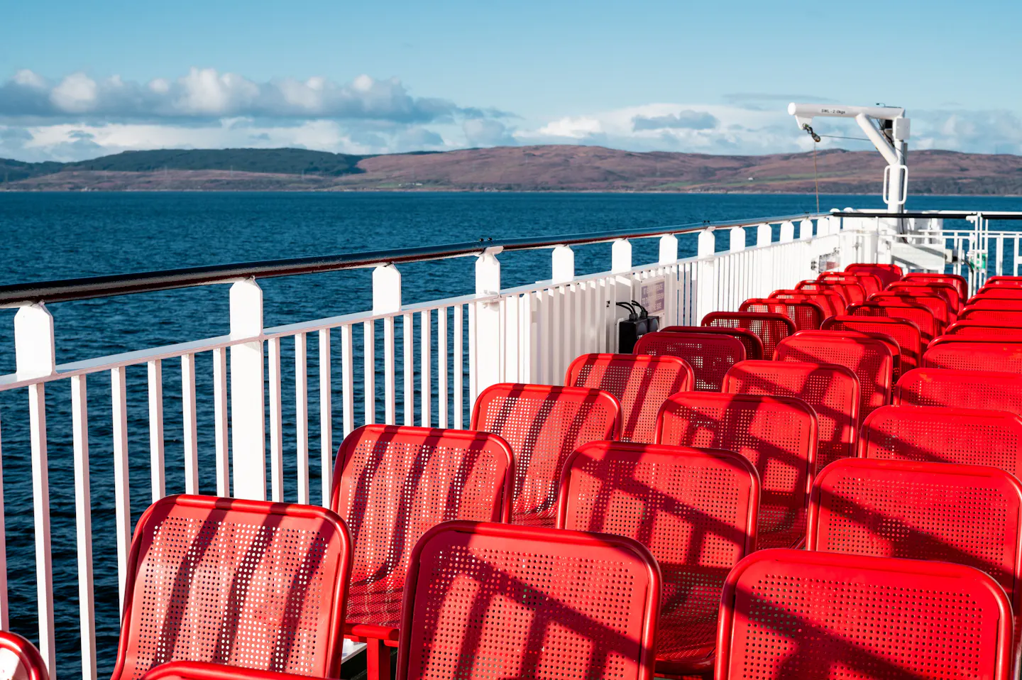 Red seats on the sunny deck of a Scottish island ferry, looking across the sea to heather hills