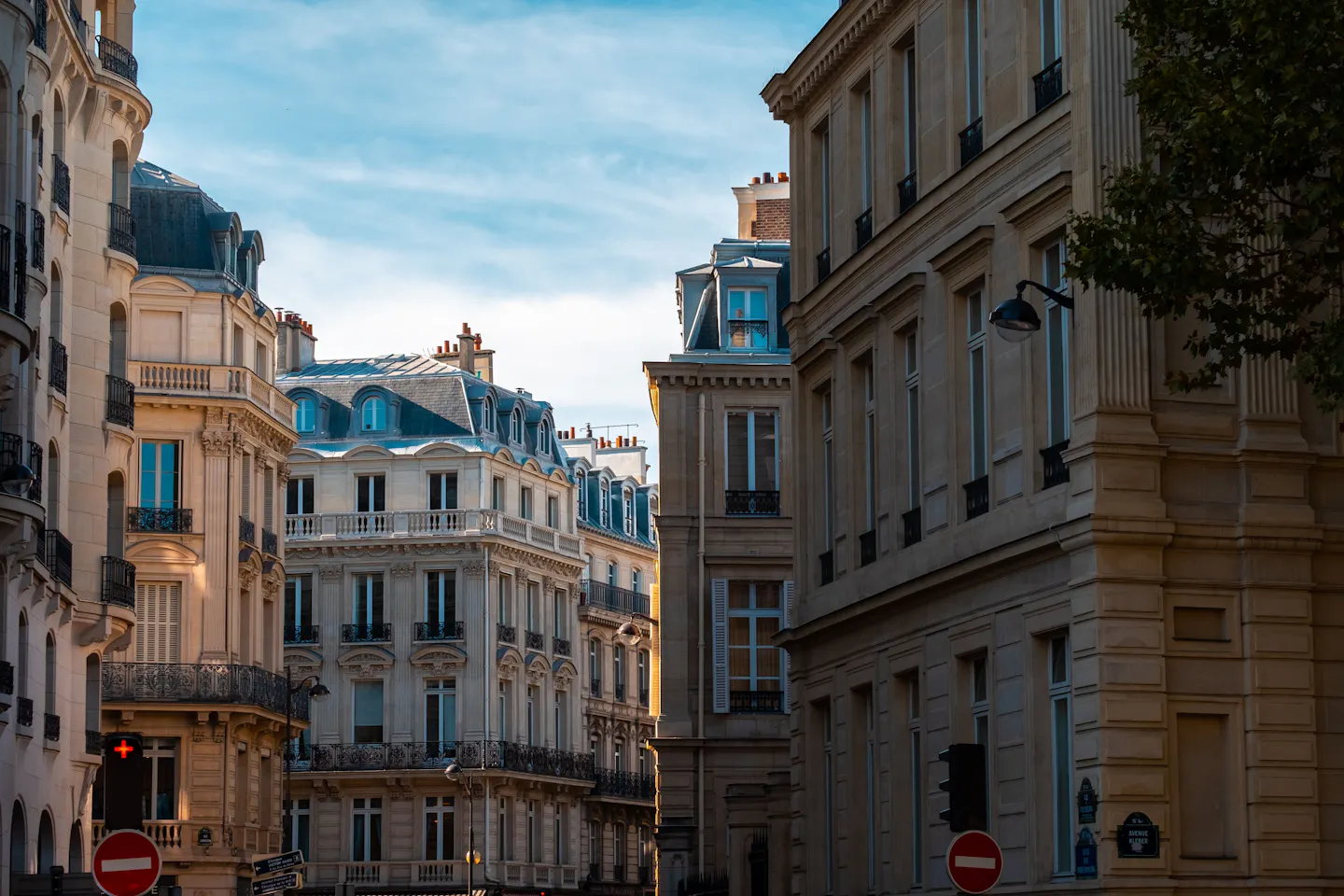 Haussmann apartment buildings with mansard roofs and balconies on a Paris street corner in warm light