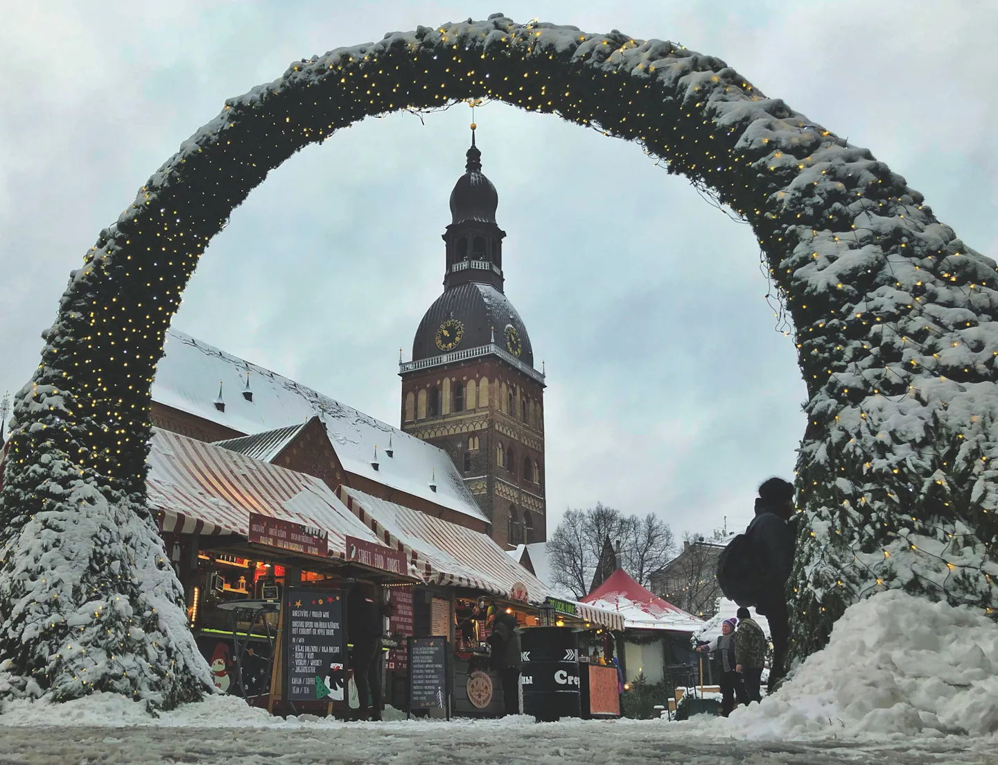 Snowy Christmas market stalls beneath the tower of St Peter’s Church in Riga