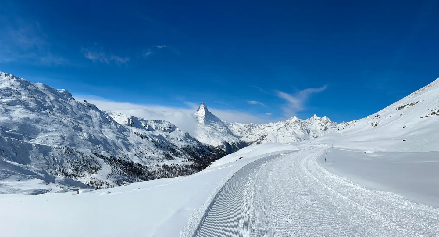 A groomed ski piste running below the Matterhorn above Zermatt under a deep blue sky