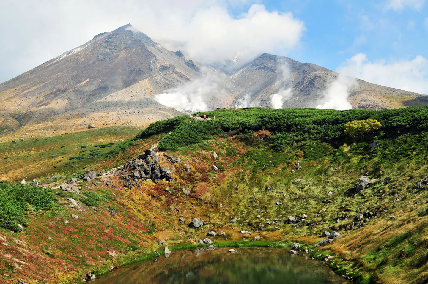 Steam venting from the flanks of Mount Asahidake in Hokkaido above a crater pond and slopes turning red and gold in early autumn