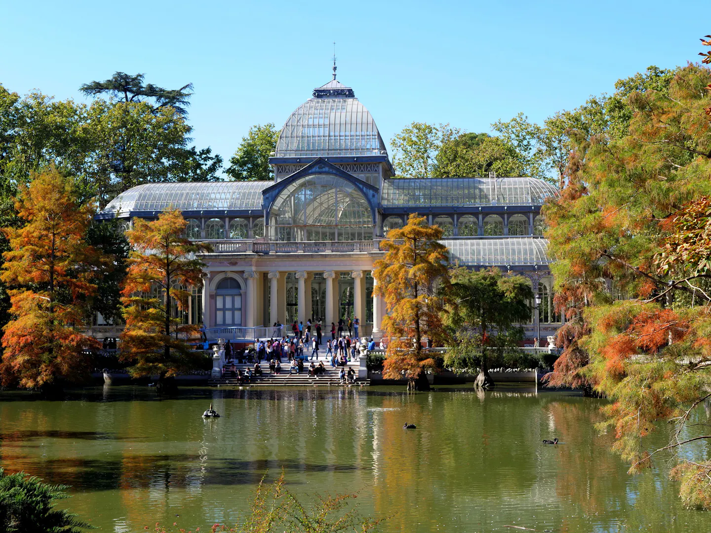 The glass Palacio de Cristal reflected in its lake in Madrid's Retiro Park among autumn trees