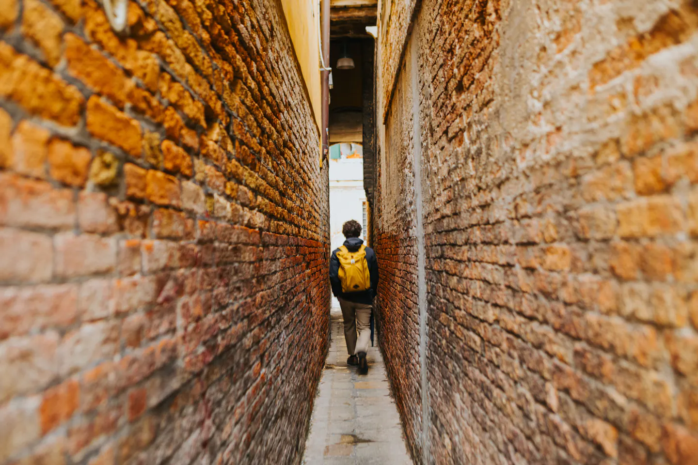 Traveler with a yellow backpack walking through a narrow brick alley