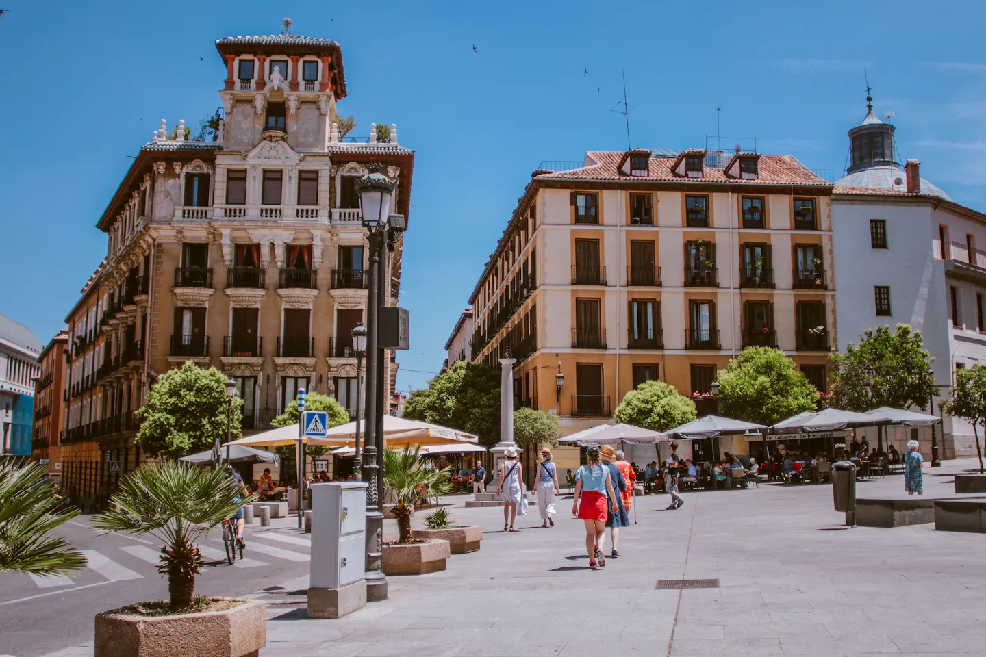 People walking past cafe terraces and shaded umbrellas in a sunlit Madrid square