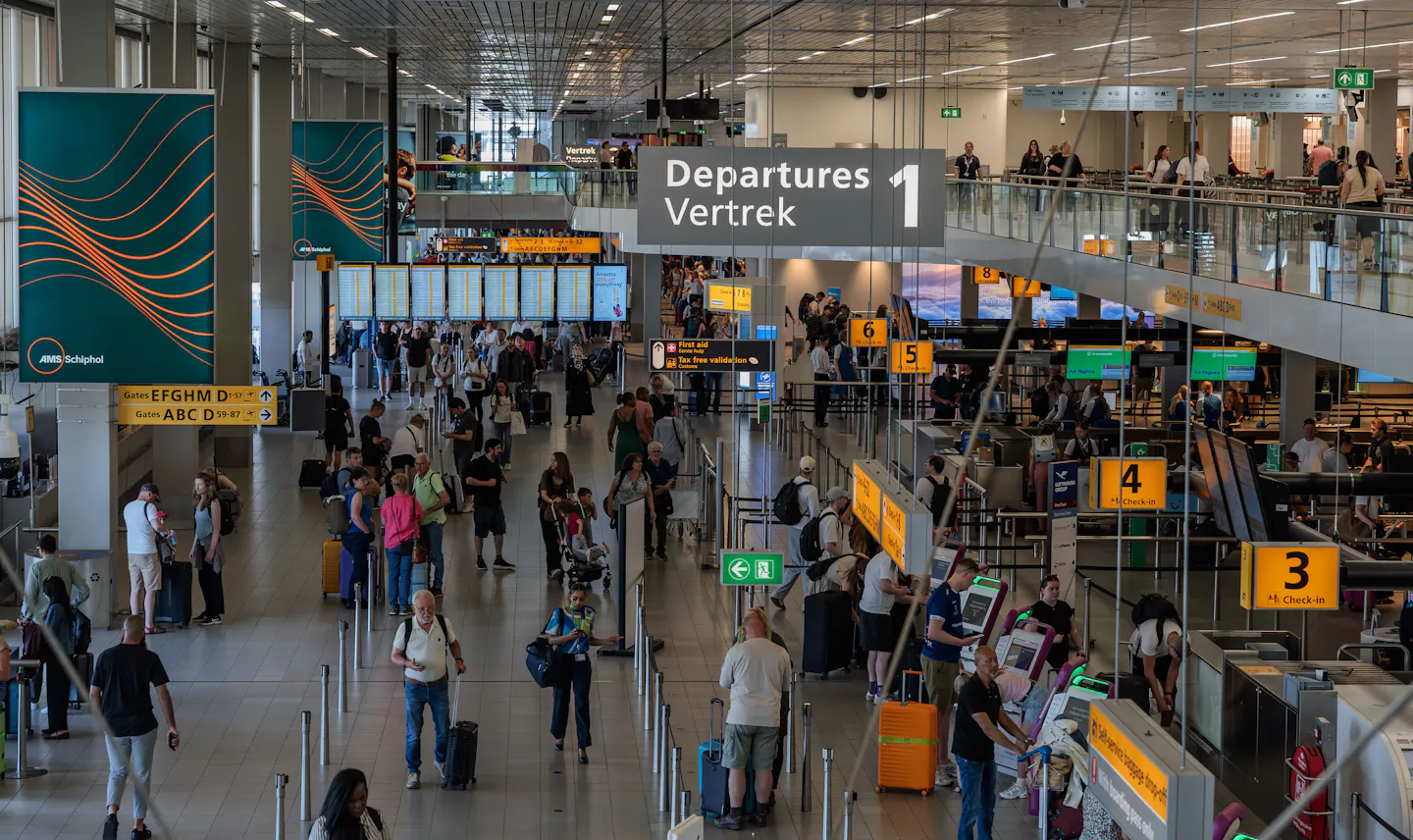 Passengers queuing at check-in counters in the departures hall at Amsterdam Schiphol Airport