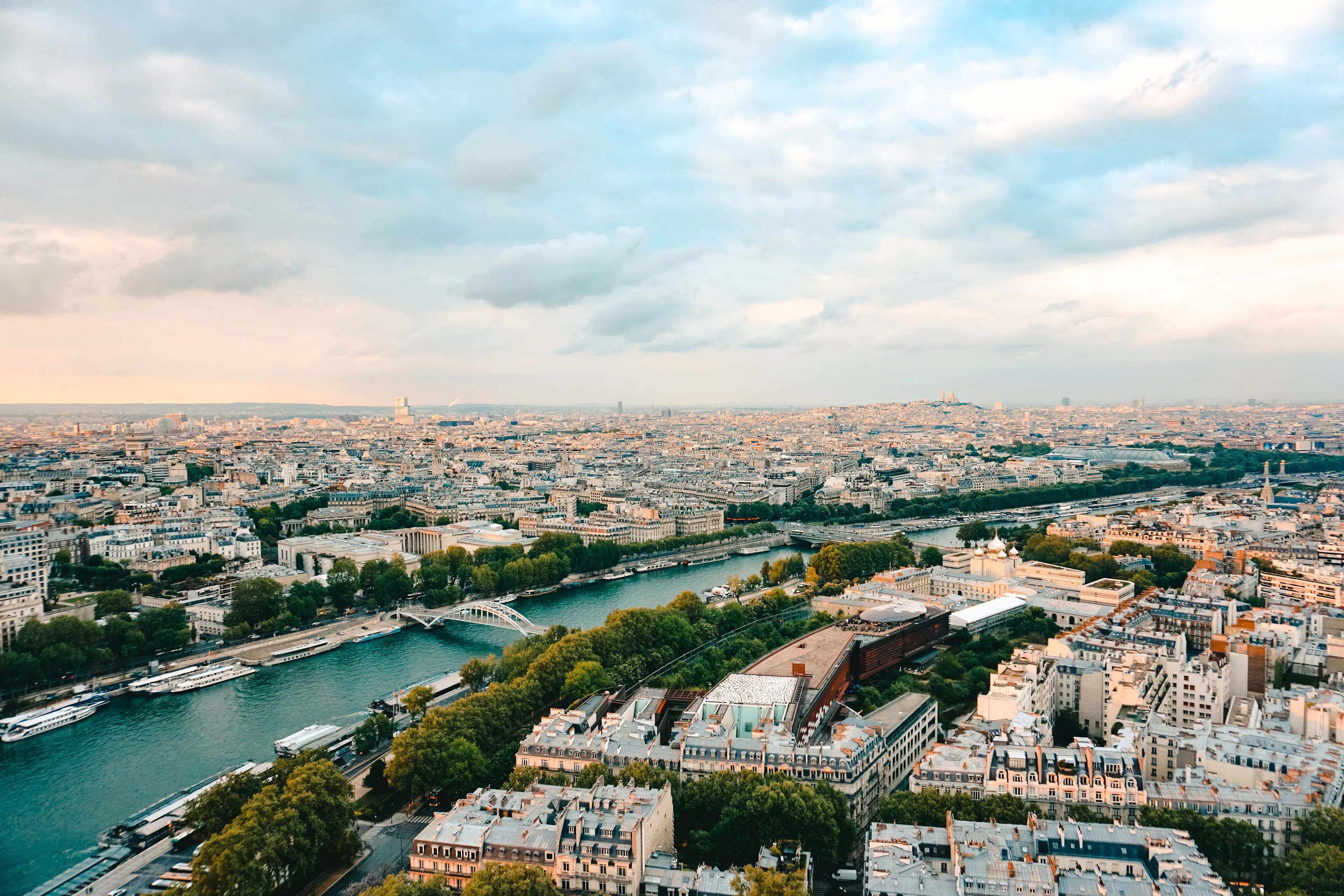 Aerial view over central Paris at golden hour, with the Seine curving between tree-lined quays and dense rooftops