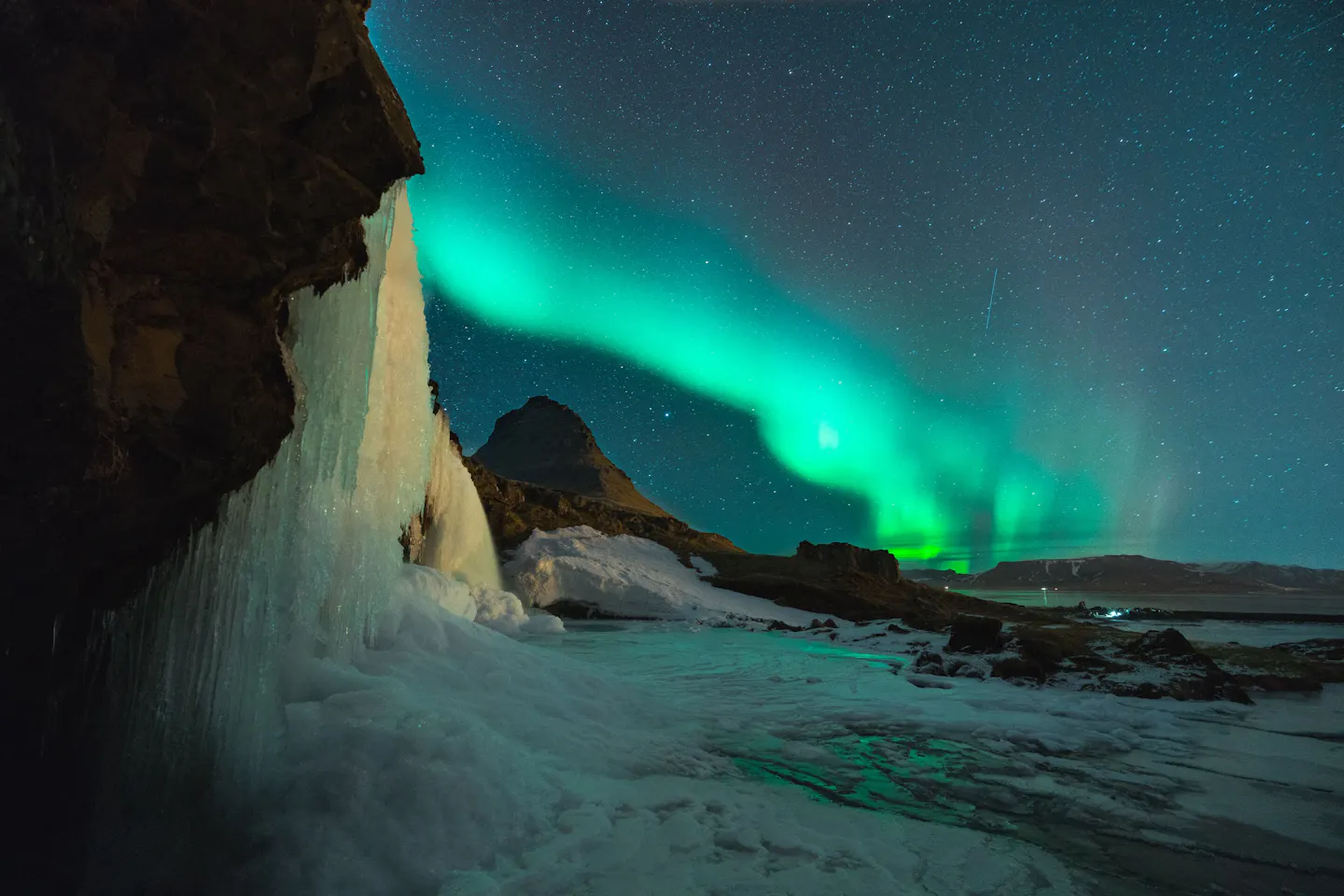 Green aurora above the frozen waterfall and pointed Kirkjufell mountain in western Iceland